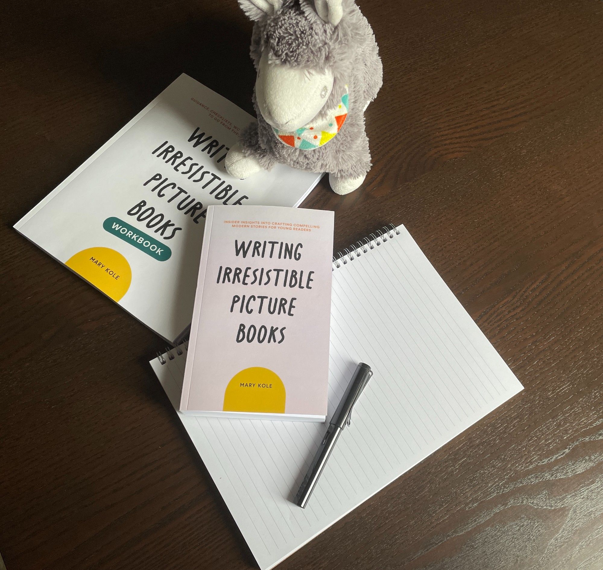 Photograph of Writing Irresistible Picture Books, a stuffed lama, a notepad and a fountain pen.