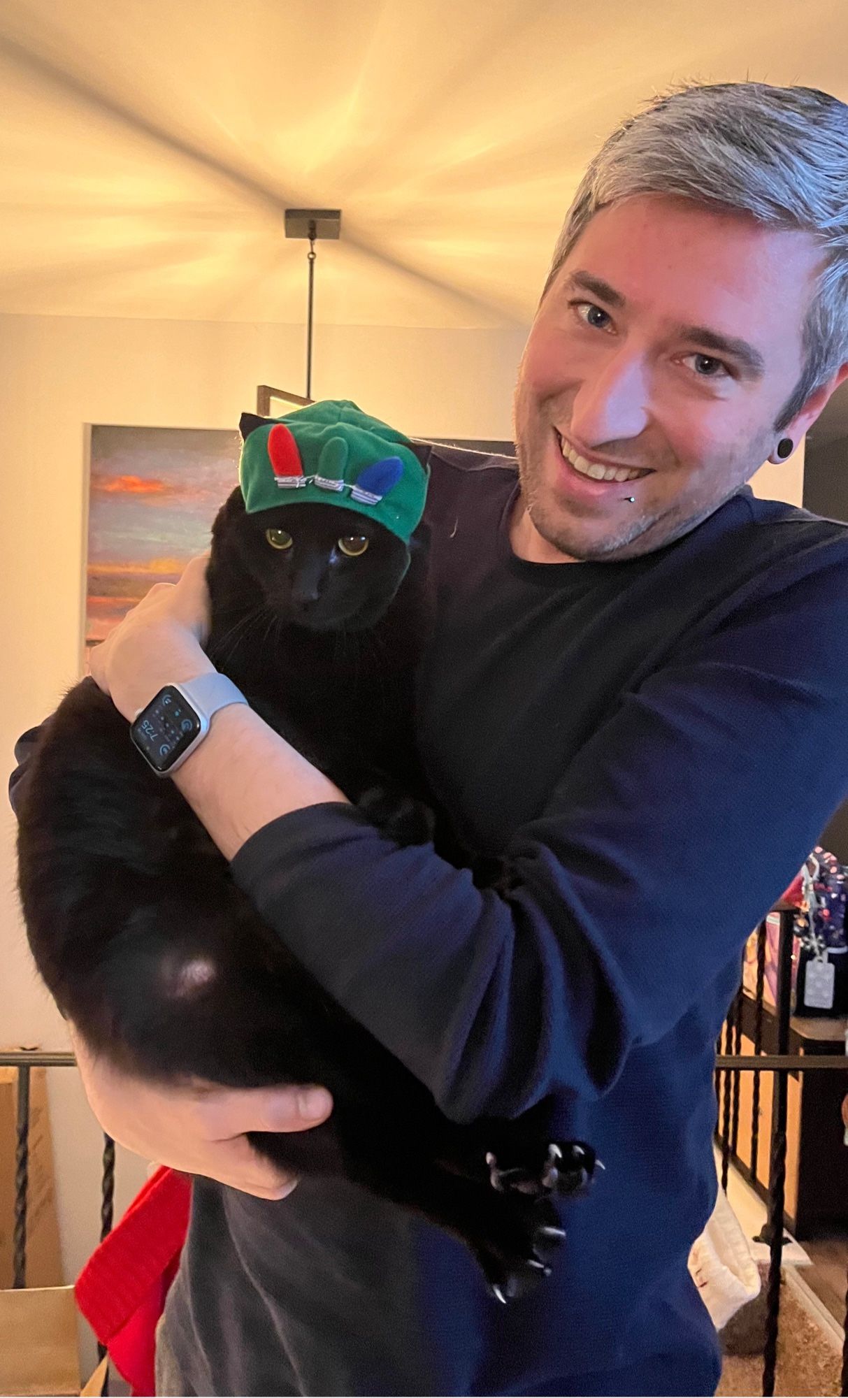 A man holding a cat with a Christmas themed hat on. The cat does not appear pleased.