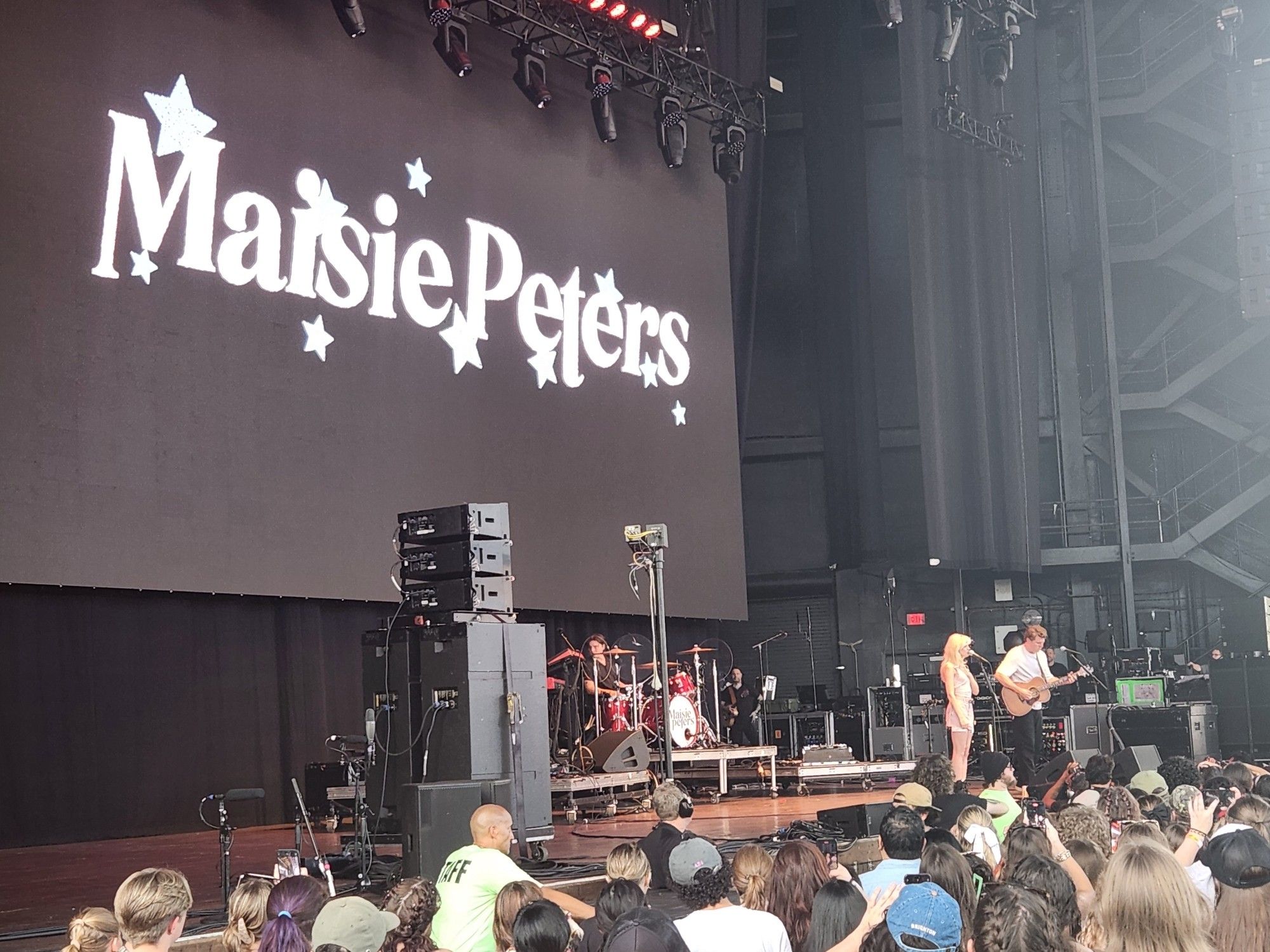 Music band Maisie Peters performing on stage in front of crowd.