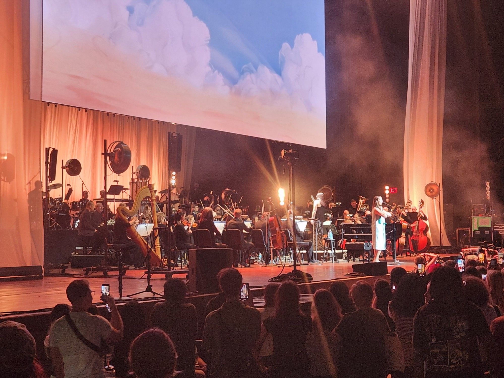 Music artist Laufey performing on stage with an orchestra in front of crowd.