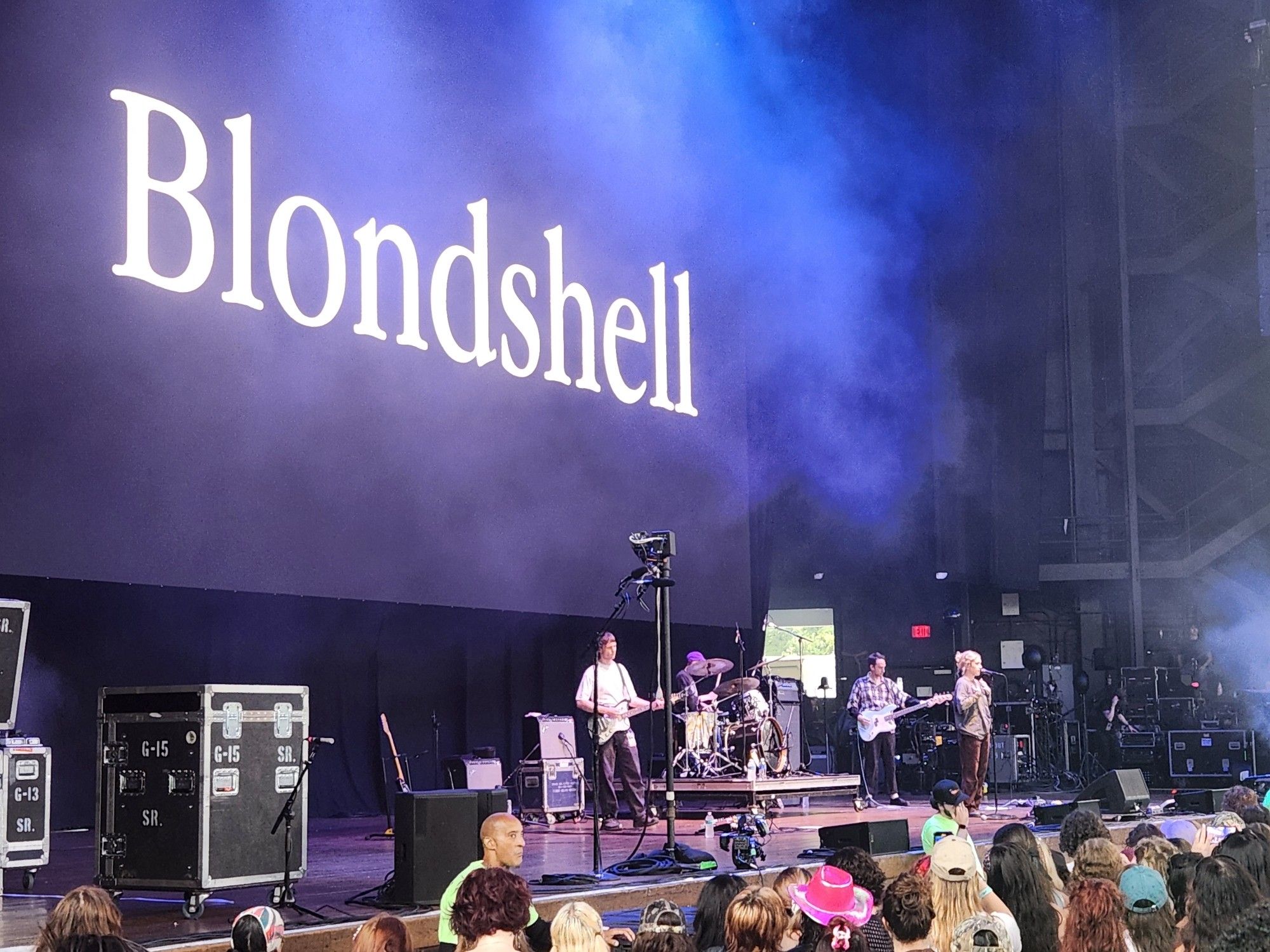 Music band Blondshell performing on stage in front of crowd.