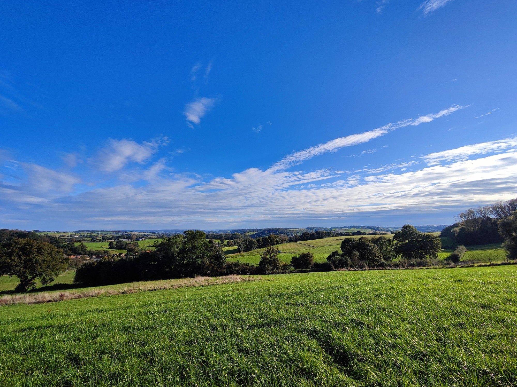 Een groen heuvelachtig landschap met daarboven een stralend blauwe lucht met in de verte wat witte wolken.