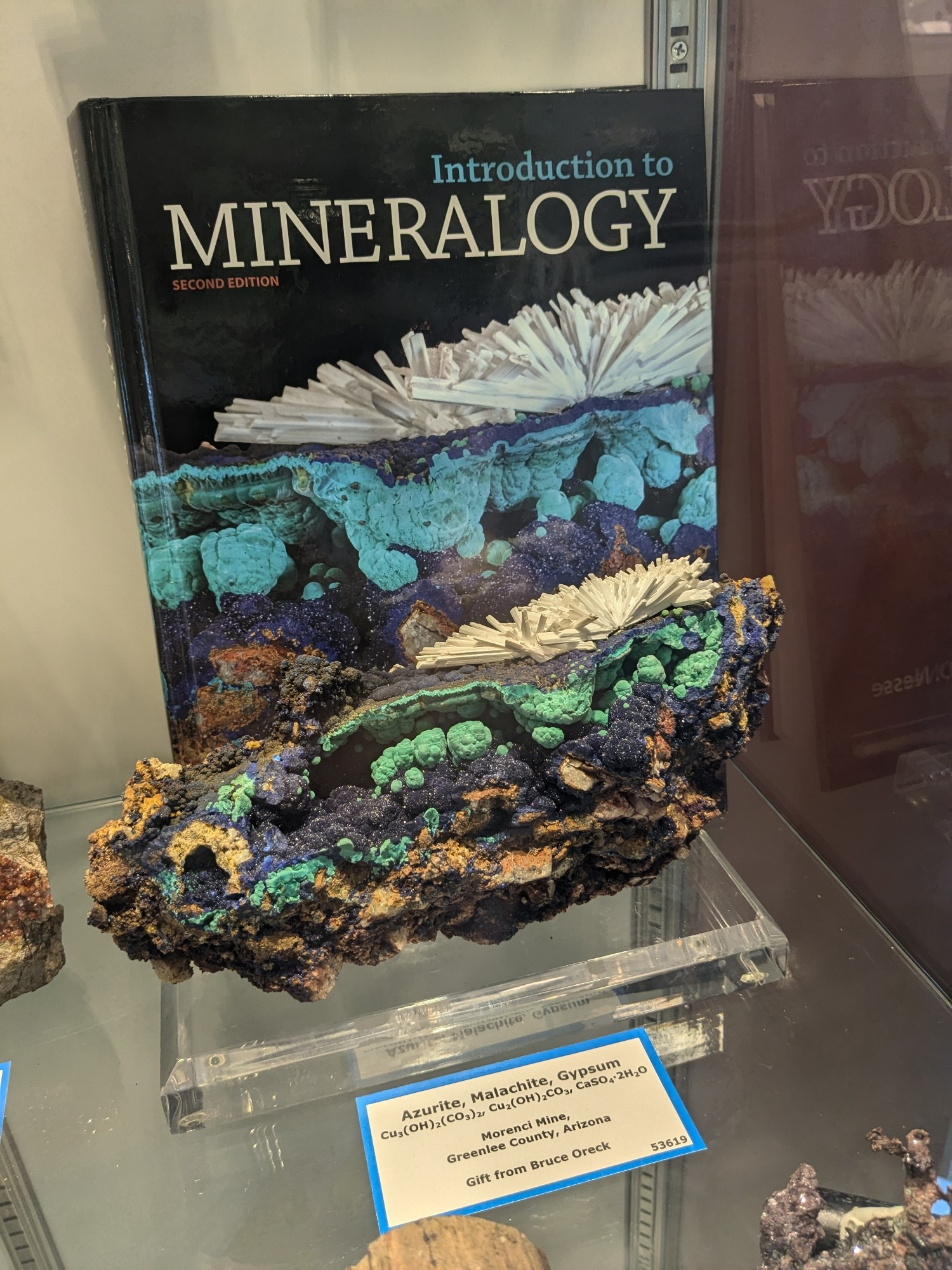 a large rock with blue and white crystals on it with a book behind it with a photo with the same crystal on it