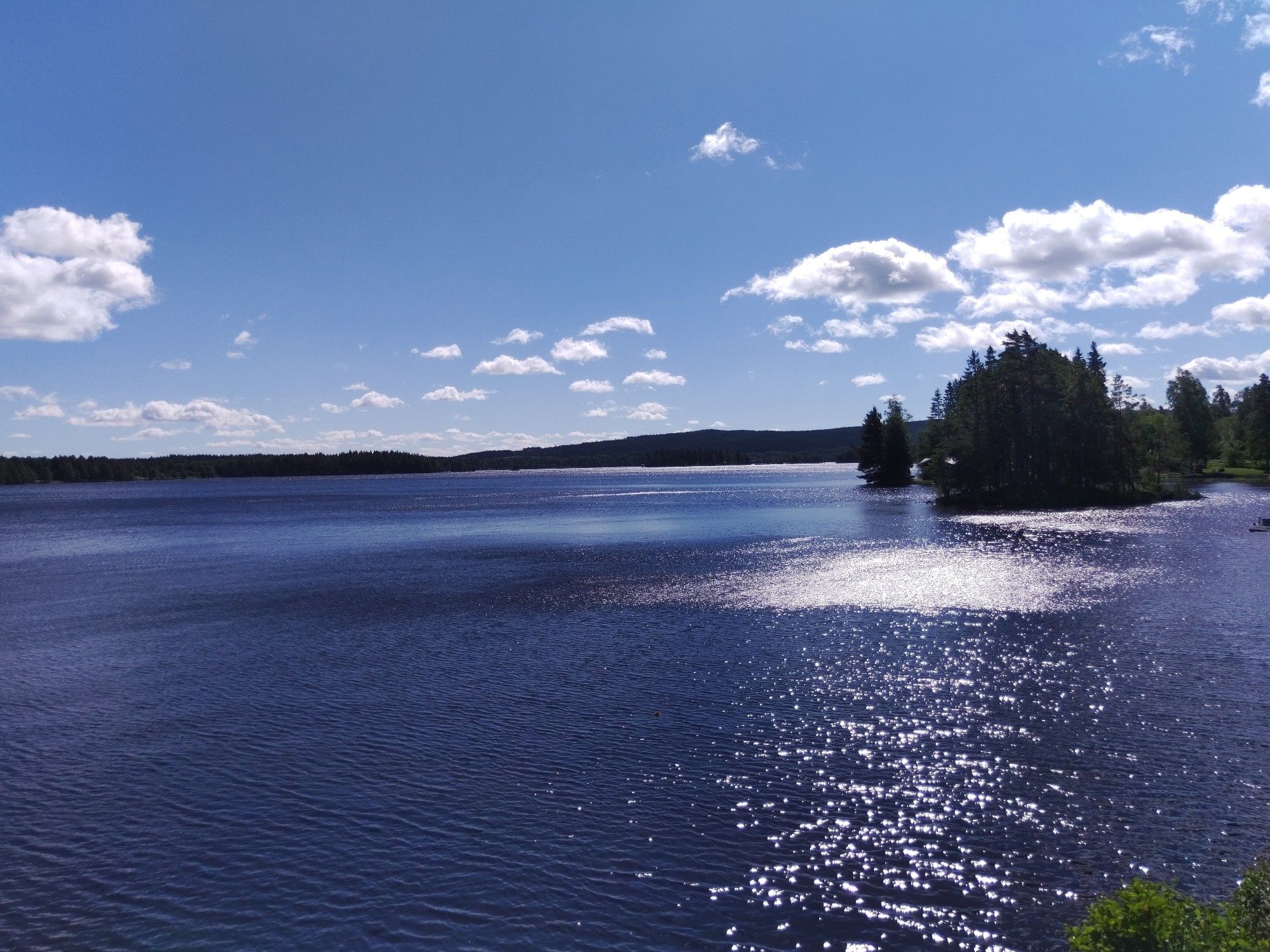 Glitzernder blauer See mit kleinen Nadelwaldinseln.