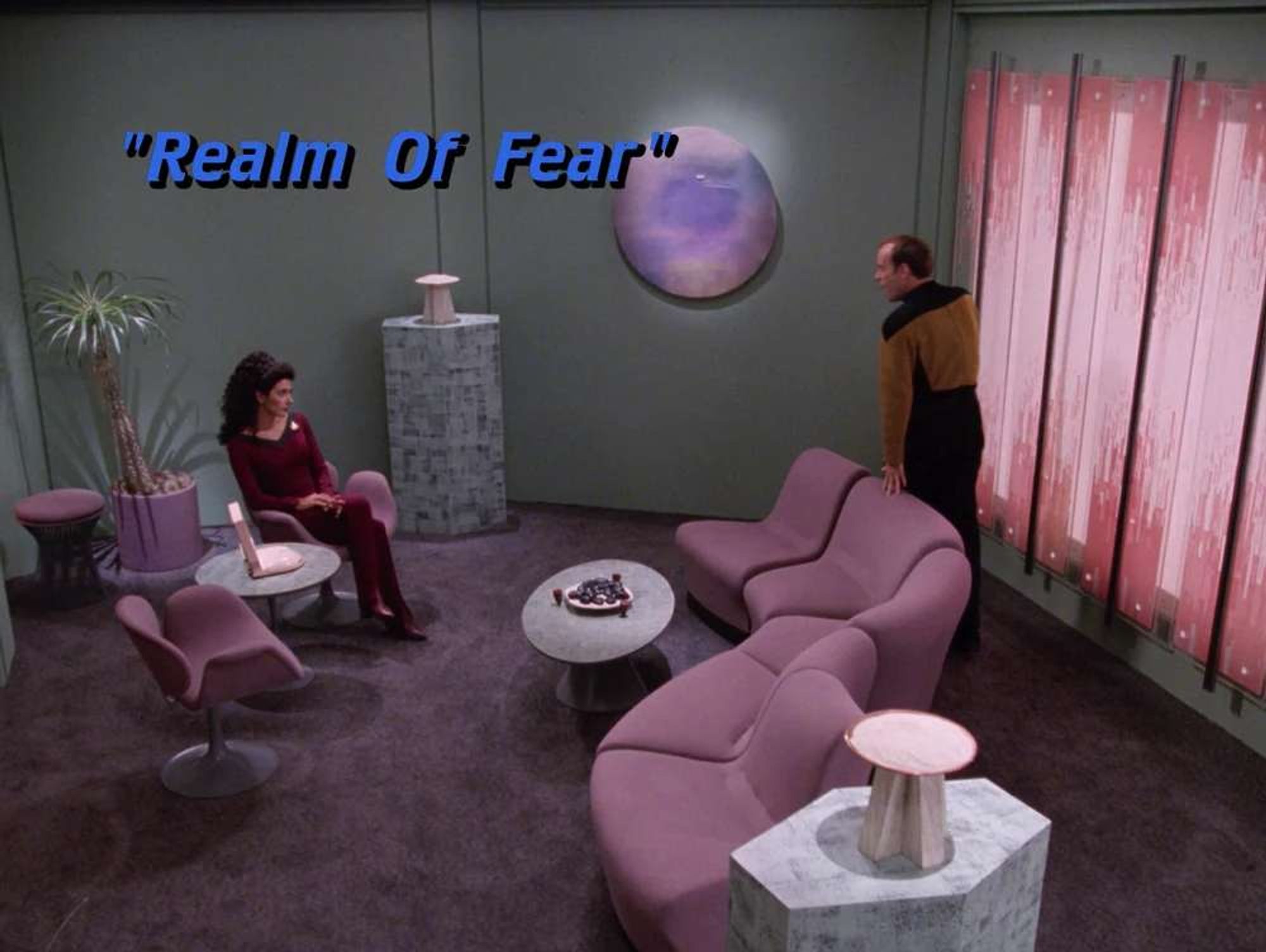 Title card "Realm of Fear." Barclay is in Troi's redesigned office, standing the couch.