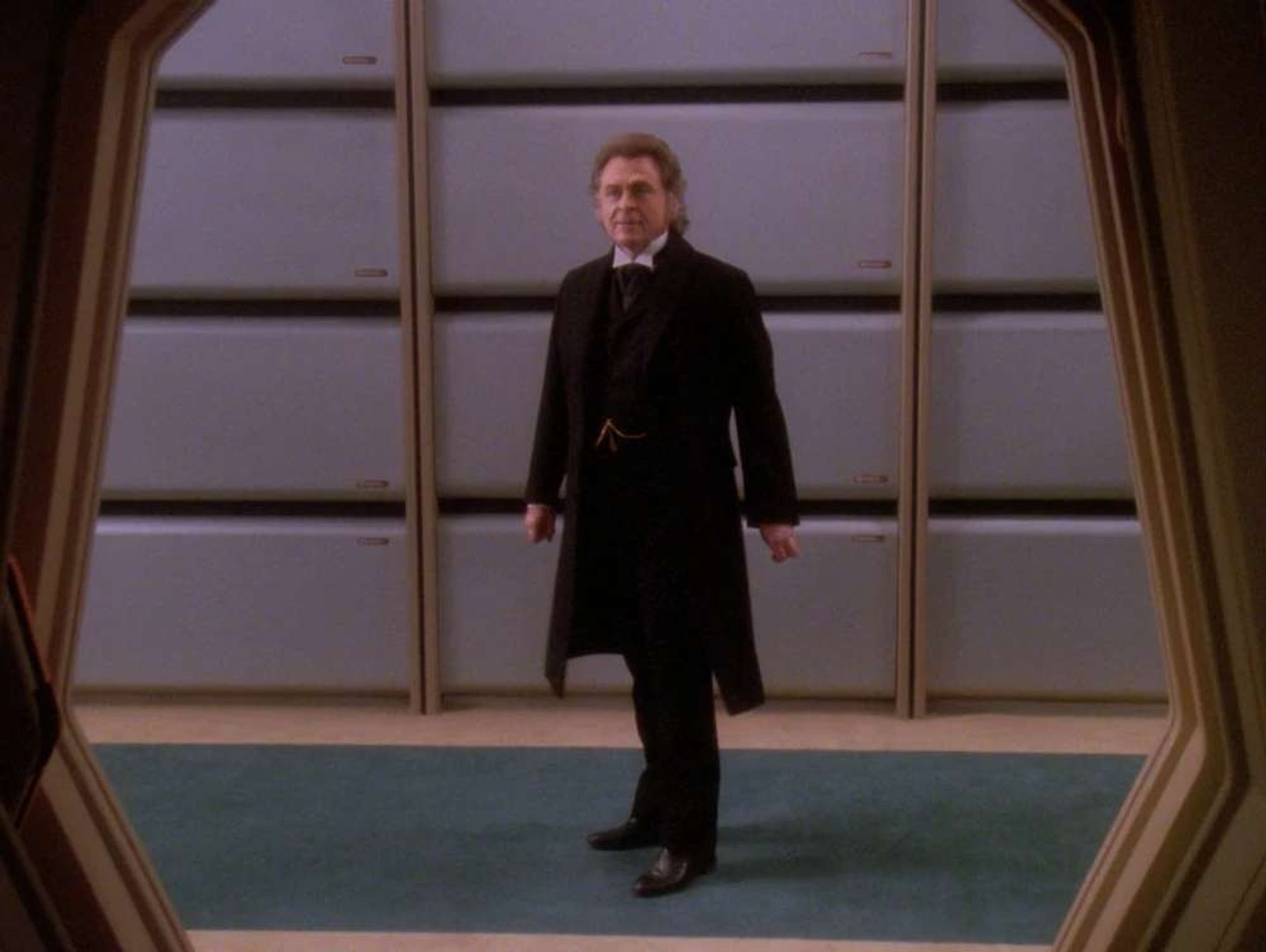 Moriarty in the Enterprise hallway after a dramatic turn, framed by the arch of the holodeck entrance.