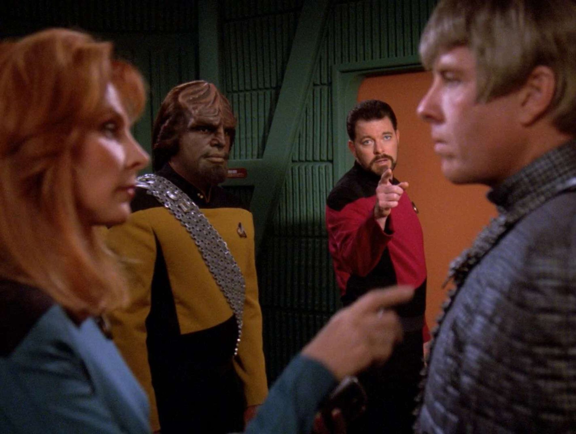 Riker pointing at the Federation defector as Worf and Crusher look on in the transporter room.