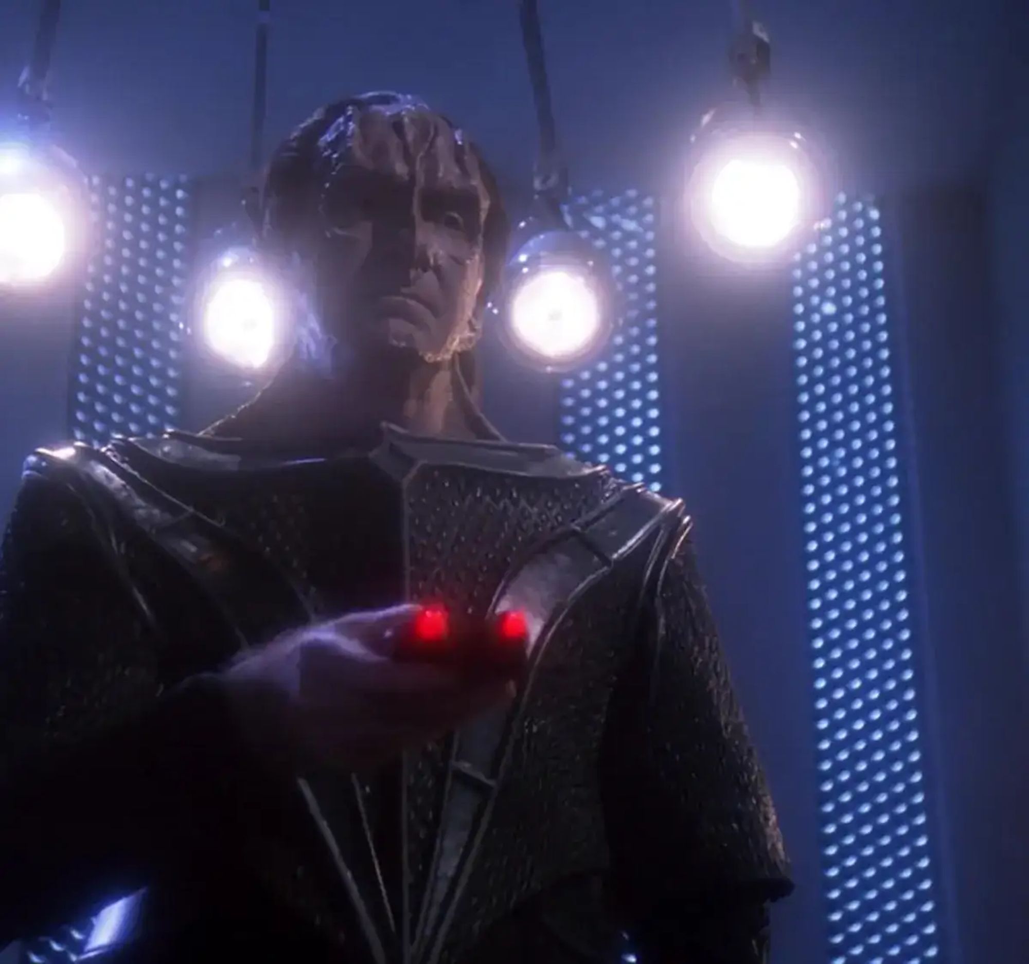 Gul Madred pointing his torture remote with four lights behind him.