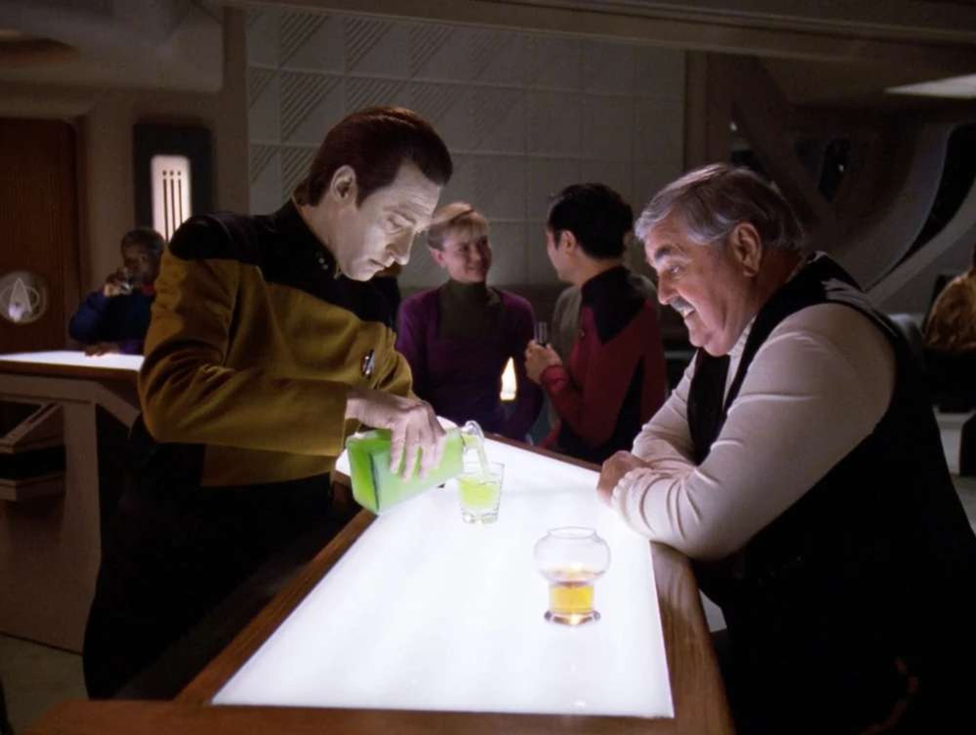 Data as bartender in Ten Forward serving Scotty green liquid.