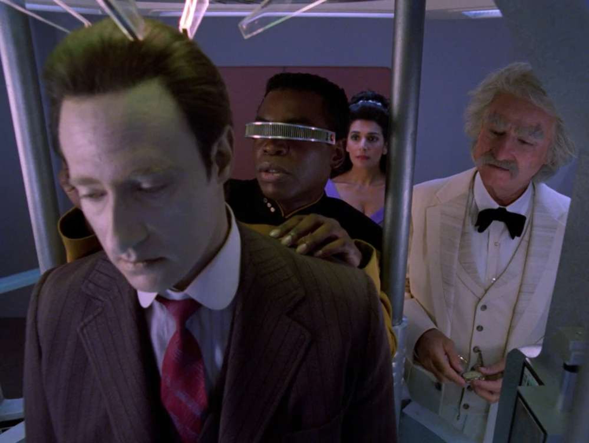 Data's head being work on by Geordi in the lab as Twain and Troi look on.