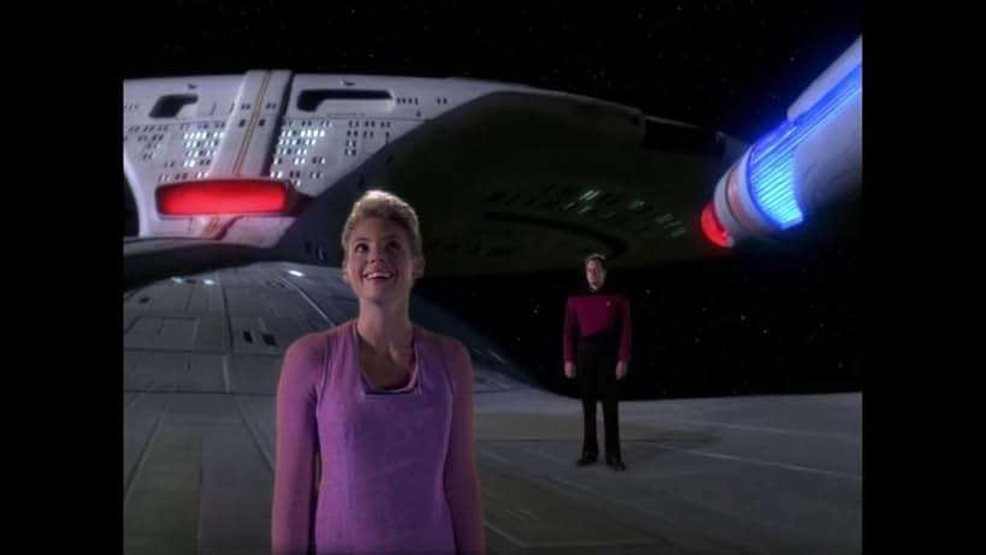 Amanda smiling in wonder standing on the hull of the Enterprise between the two nacelles with Q standing far in the background.