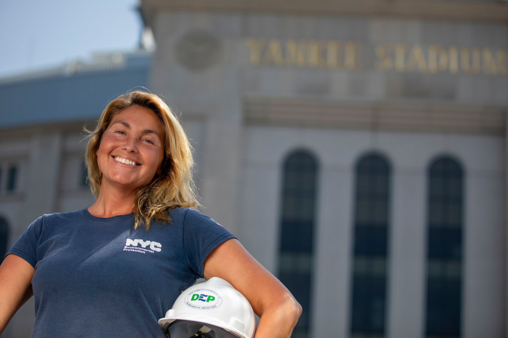 Effie Ardizzone, with a DEP t-shirt and hard hat, stands in front of Yankee Stadium.