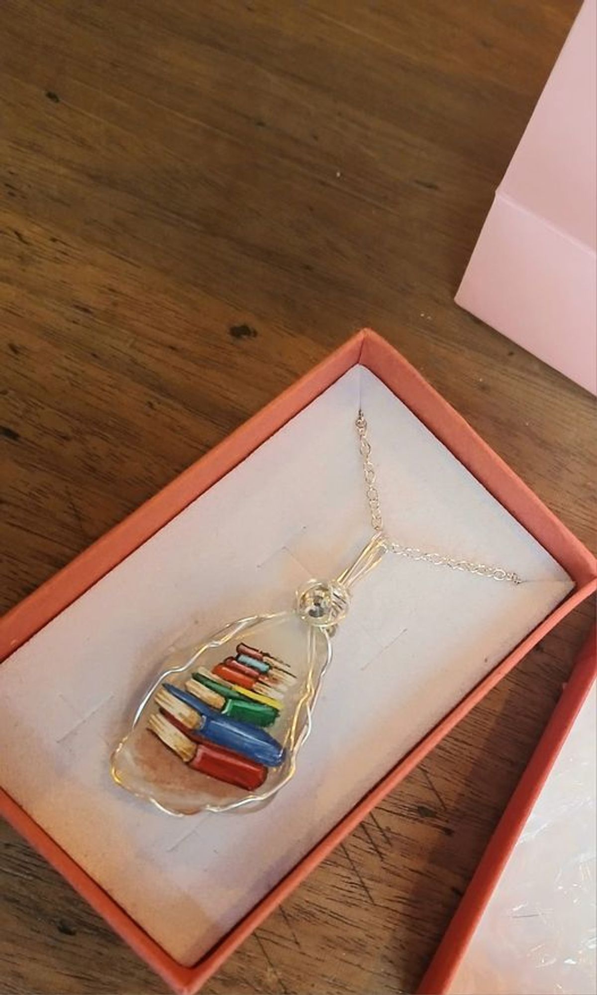 It is a painted sea glass necklace from an artisan market.  
The painting on the necklace is of a pile of books.