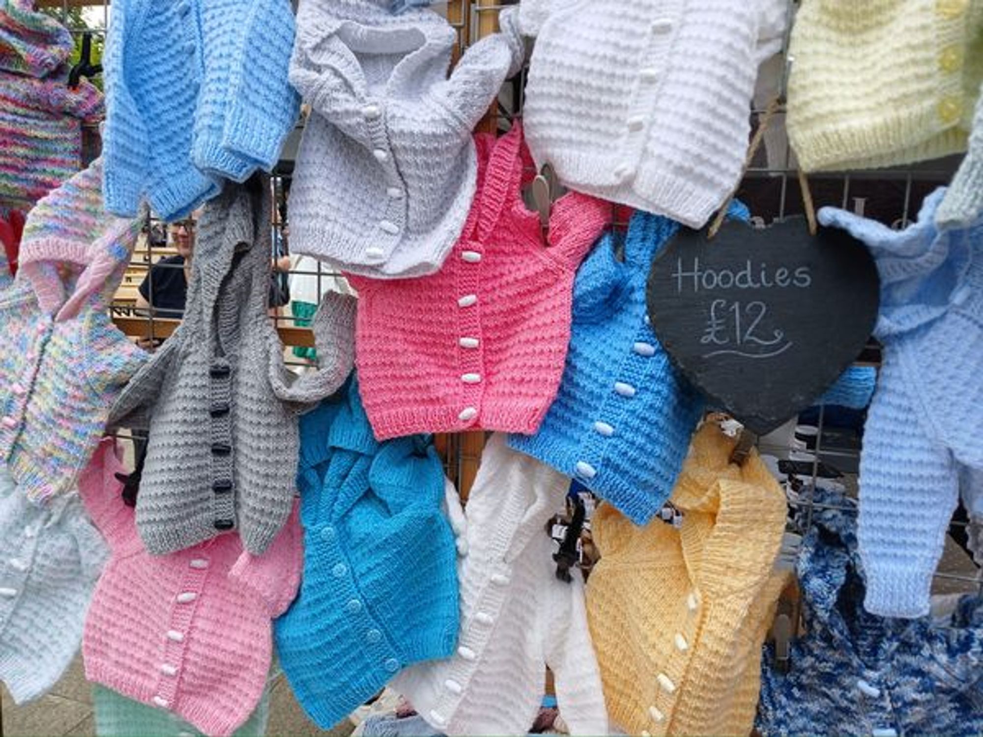 It is a colourful display of children's knitted hoodies for sale at an artisan market.