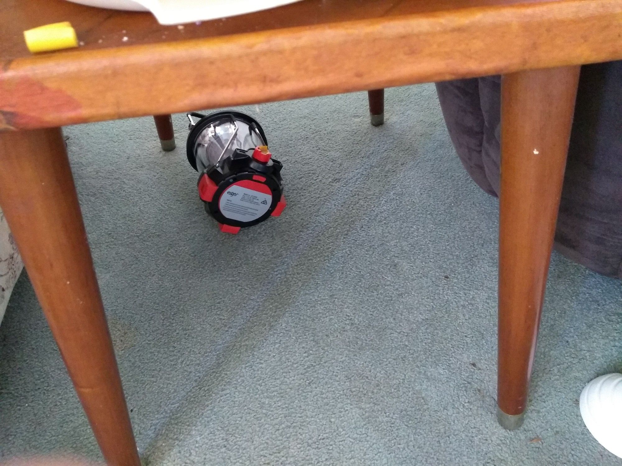 Emergency lantern tipped over by vacuum cleaner under coffee table hard to reach.