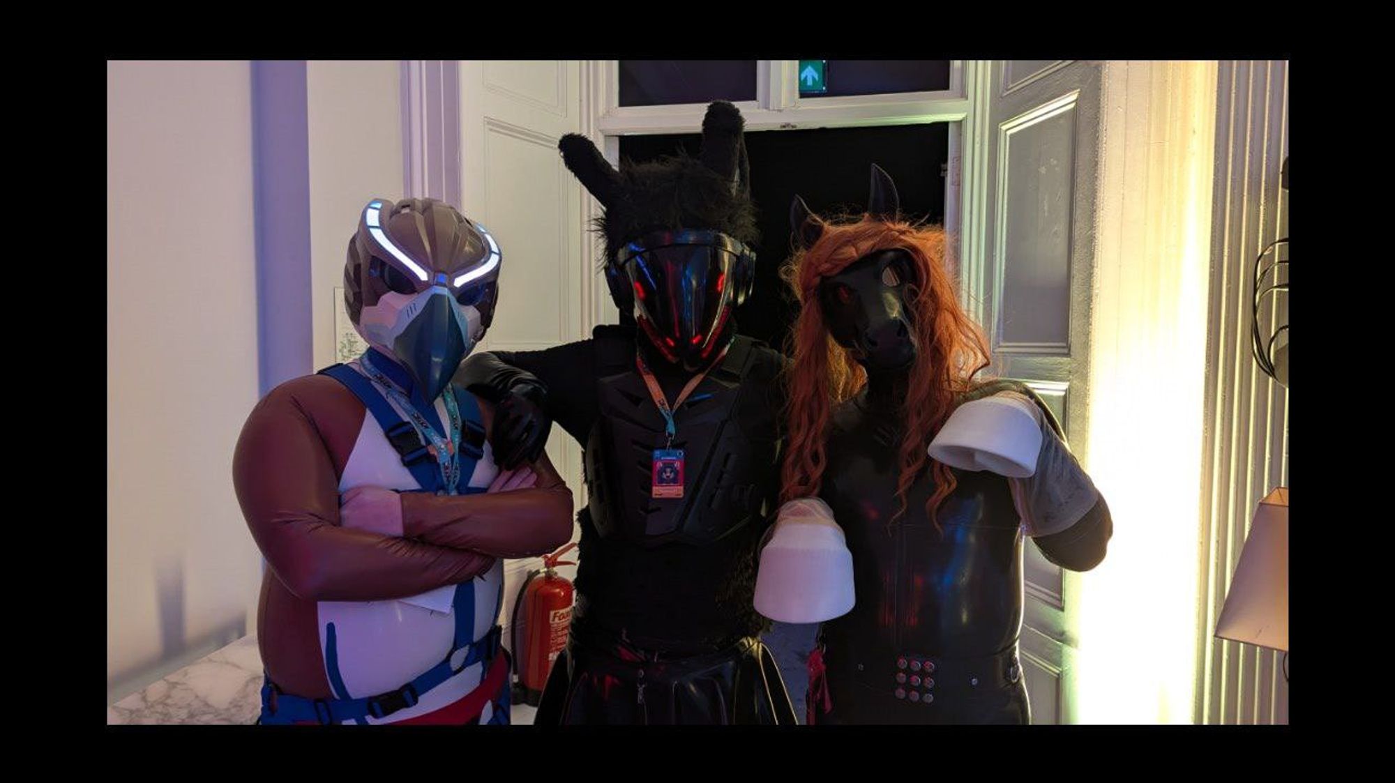 3 people in latex catsuits one in a bird drone helmet, one protogen helmet and one rubber pony