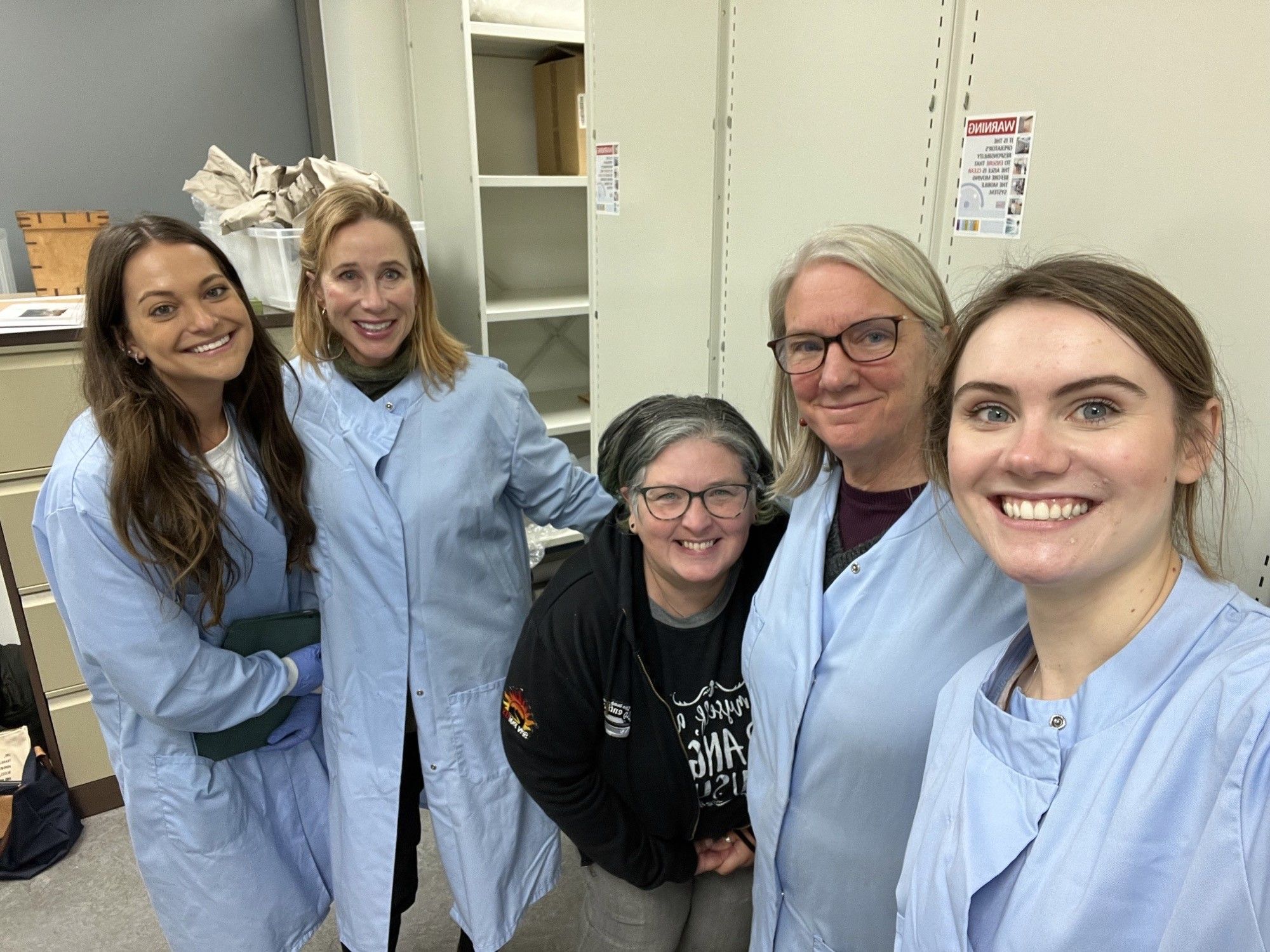 Group of 5 people, 4 in blue lab coats, with white backgound.