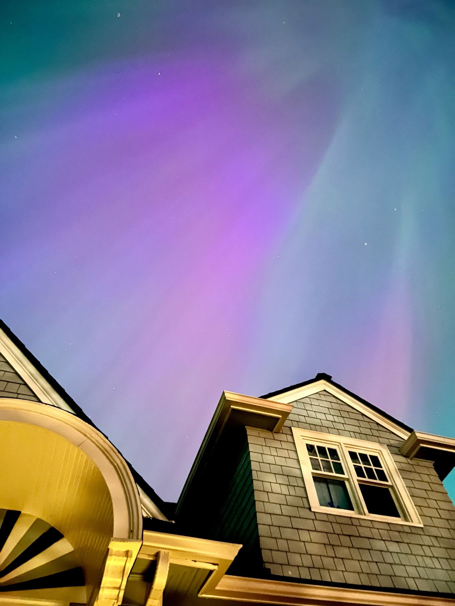 Pink and green Aurora borealis above a house.