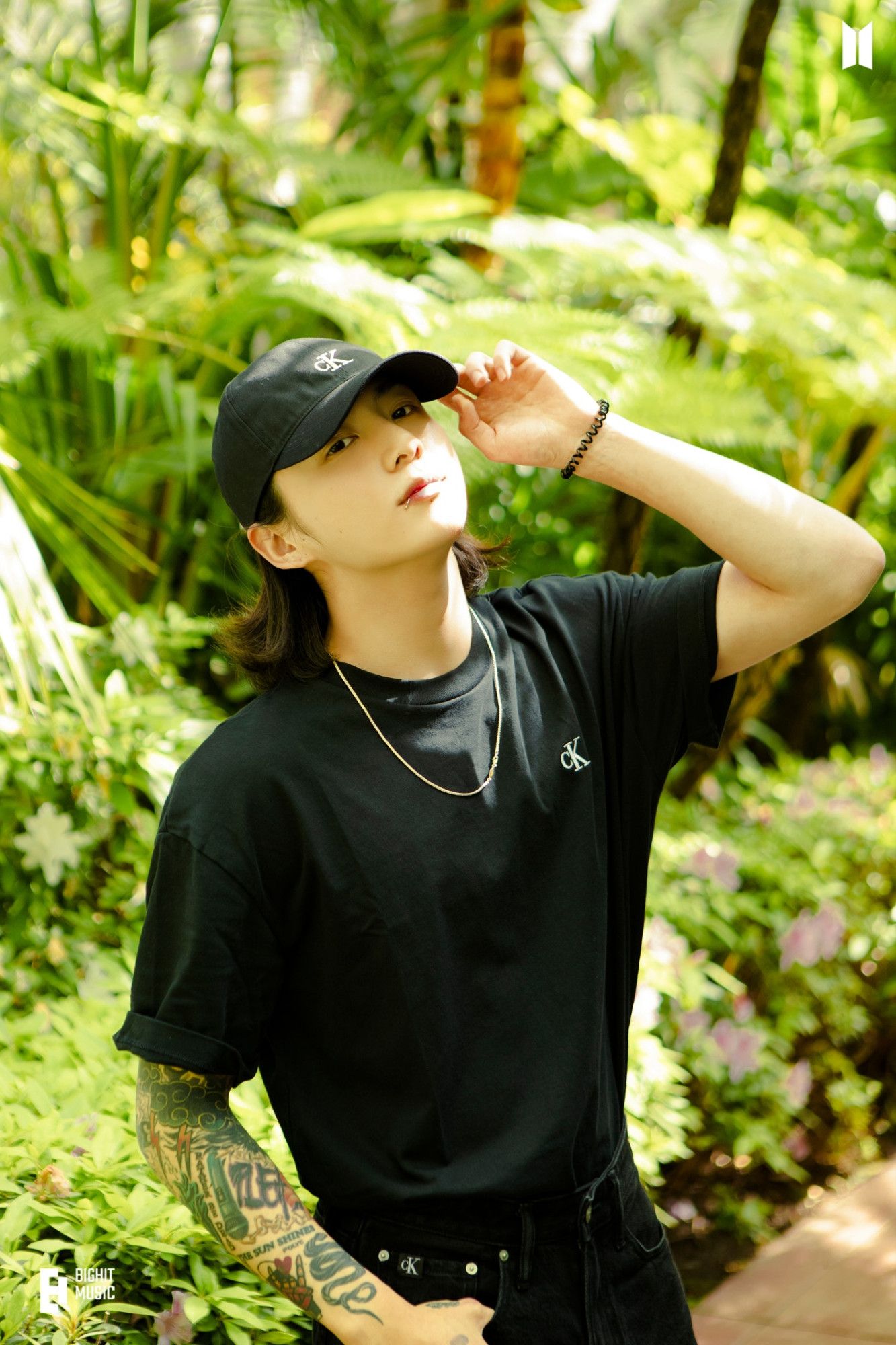 Photo of adult Jungkook from 2023, wearing a CK cap and a black t-shirt with his tattoed arm showing