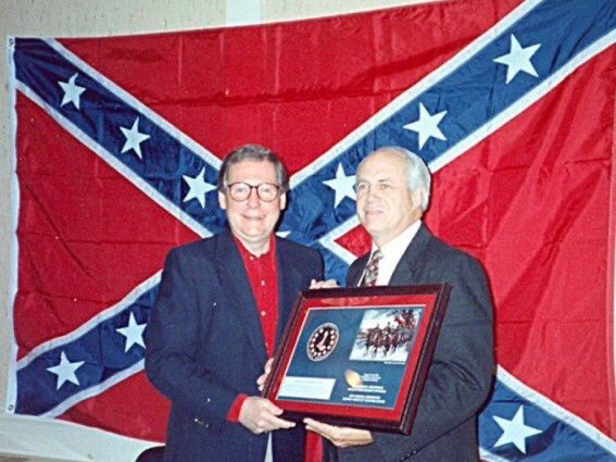 Addison “Mitch” McConnell accepting an award in front of the confederate traitor rag.