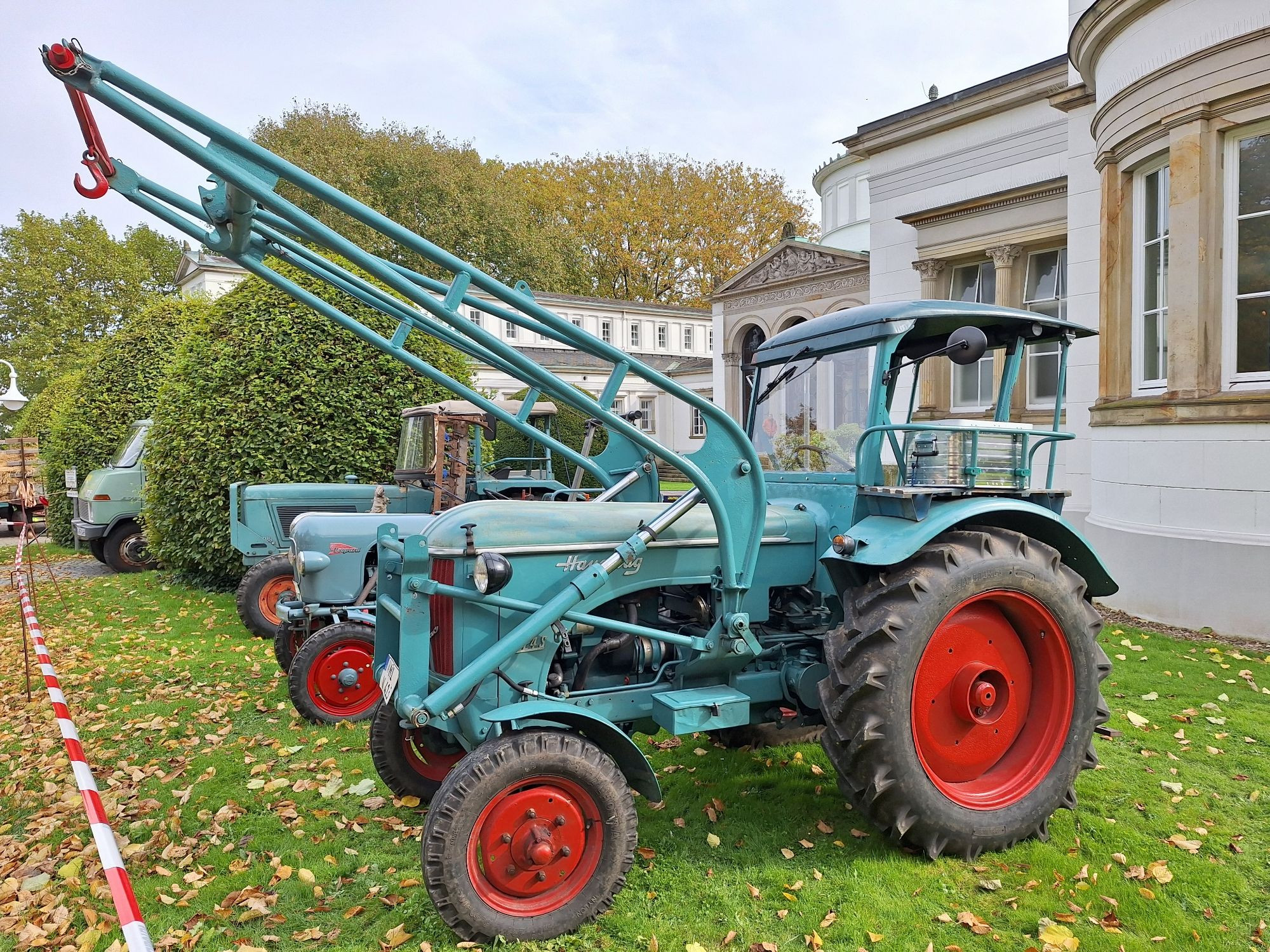 Querformat, Farbe.  Foto zeigt einen hellgrünen Hanomag Traktor mit einer Hebeanlage für z.B. eine Heugabel oder eine Schaufel. Der Fahrersitz besitzt eine Kabine. Die Felgen sind rot.