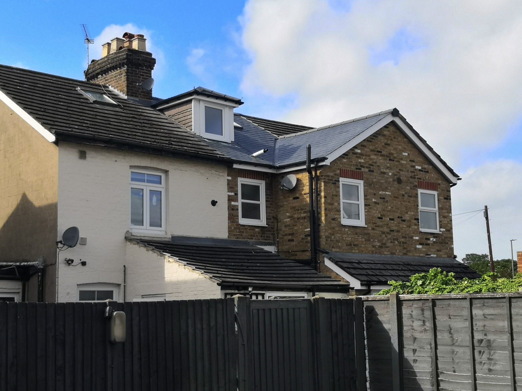 The back of some terraced houses, one of the which has slate tiles in the main roof and the extension. The others have concrete tiles.