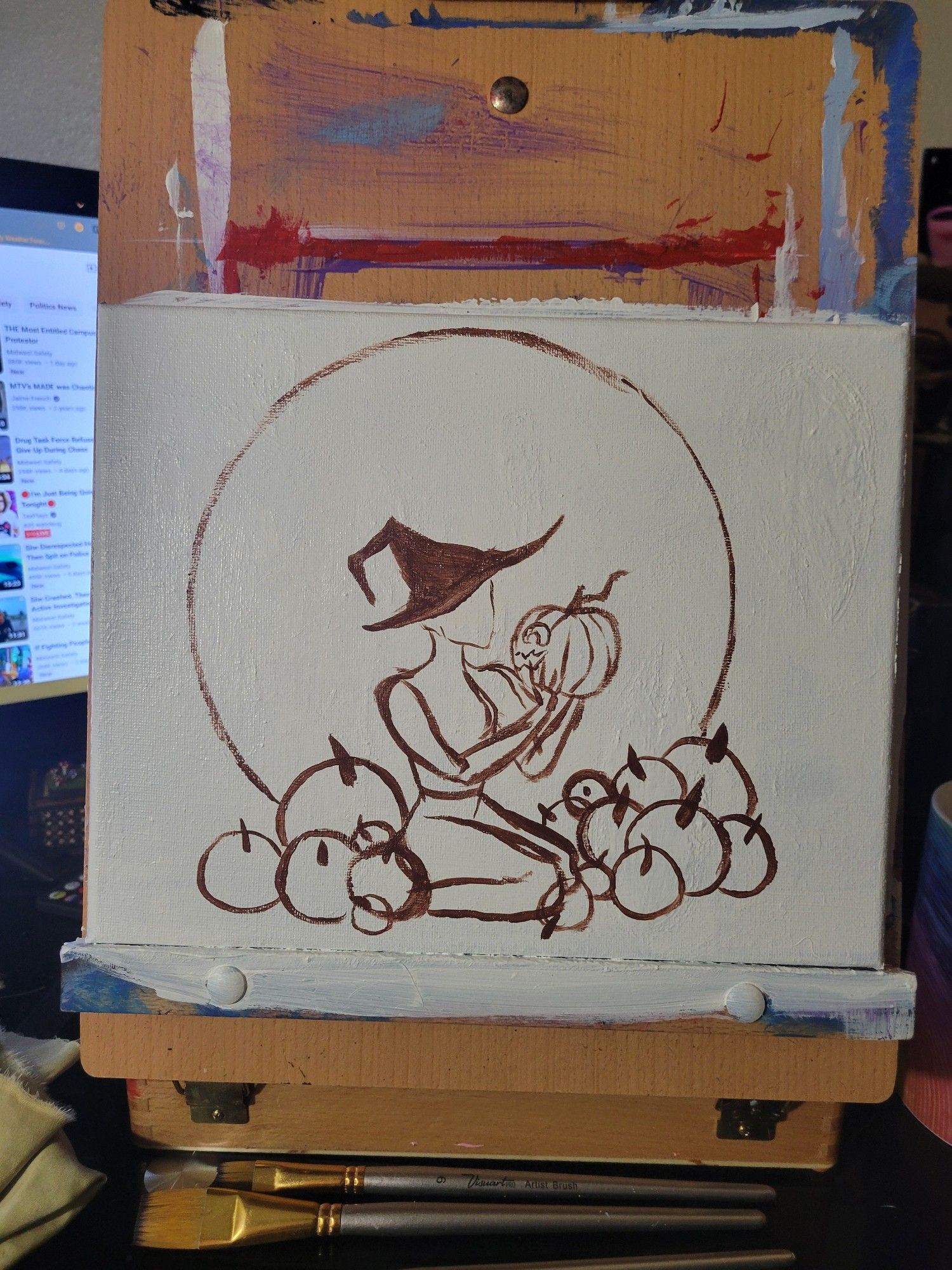 A small canvas on a desktop esael. The canvas contains a sketched outline of a large moon with a witch sitting in between a pile of large pumpkins. In her hands she holds a carved jack-o-lantern.