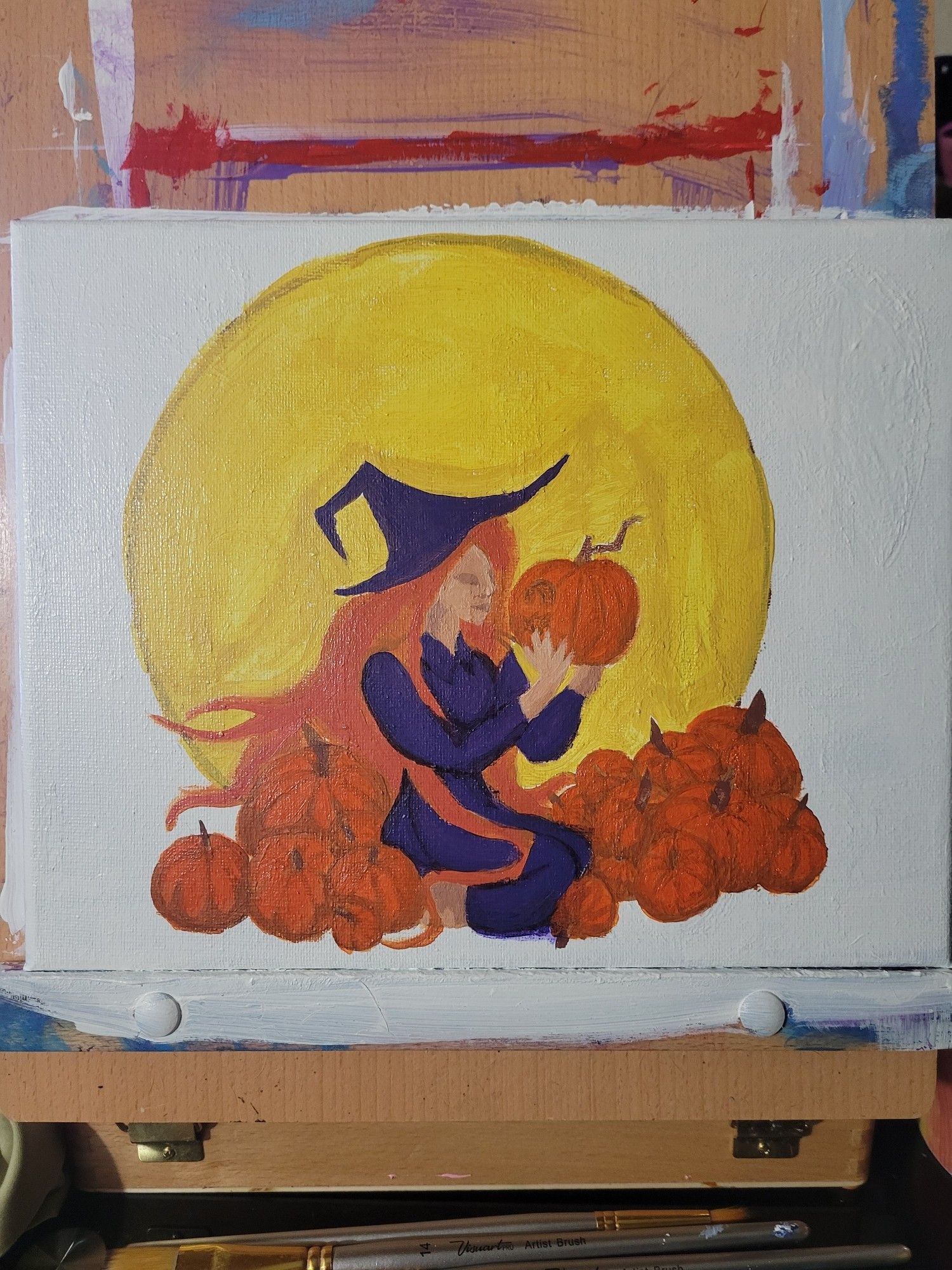 small canvas on a desktop esael. The canvas contains a rough flat painting of a large moon with a witch wearing a purple dress sitting in between a pile of large pumpkins. In her hands she holds a carved jack-o-lantern held up to her face as she gazes into the lantern light.