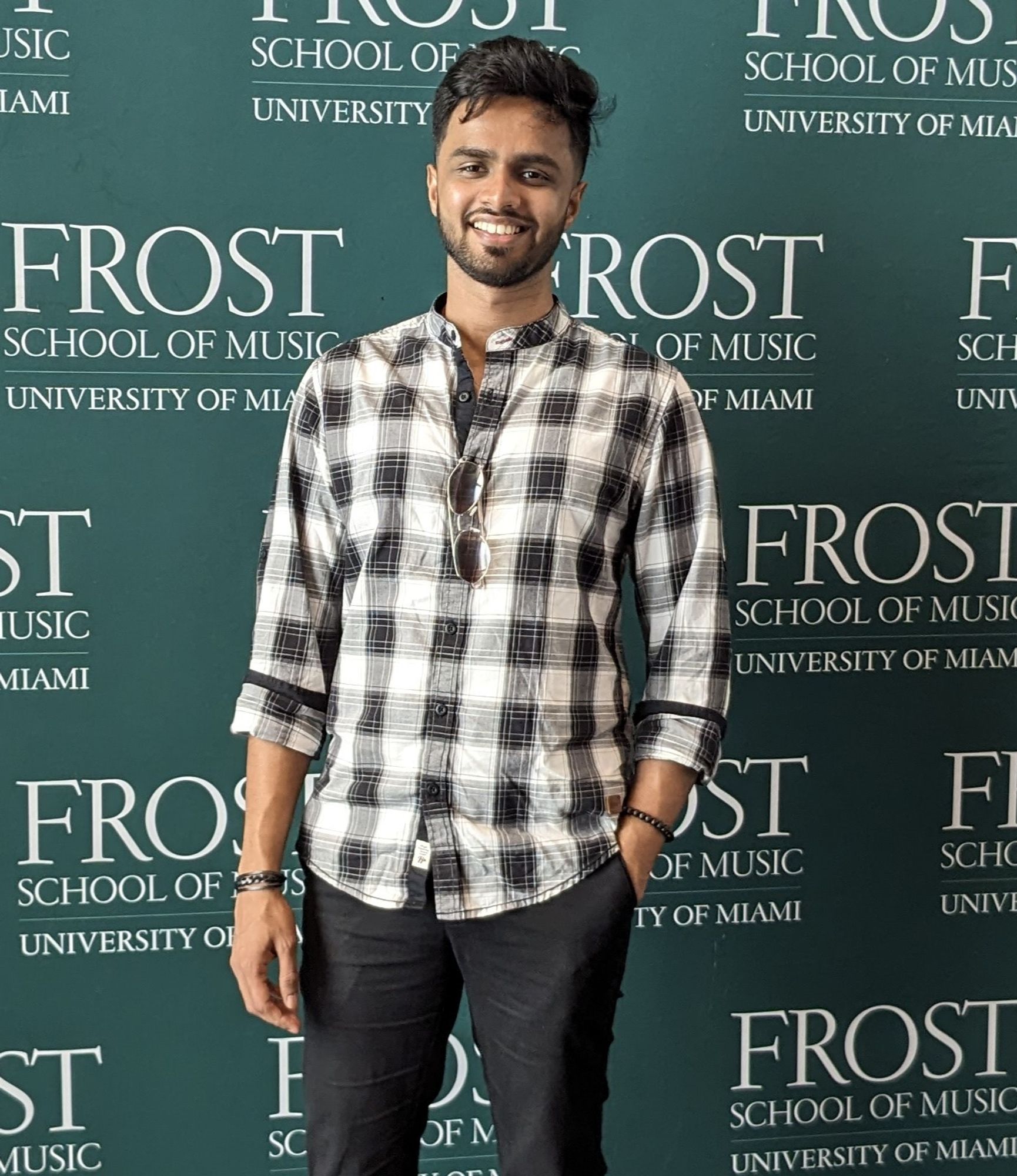 Ashay Dave, an Audio Programmer, DSP Engineer, Game and XR Developer, Musician, and a recent Master's graduate from the Music Engineering Technology program at the University of Miami, stands in front of a background that reads "Frost School of Music University of Miami"