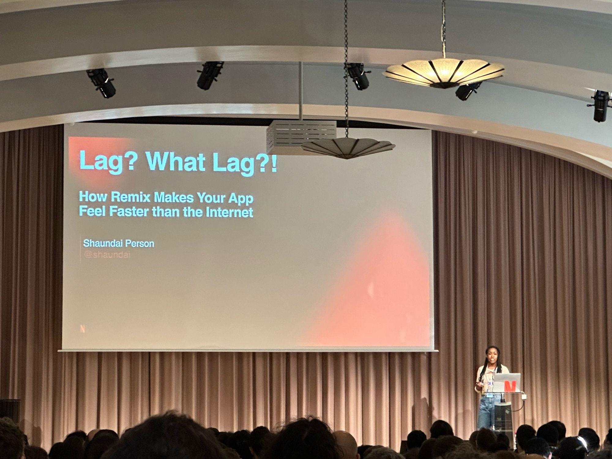 Shaundai on stage at React Paris with a title slide behind her that says “Lag? What Lag?! How Remix Makes Your App Feel Faster Than the Internet”