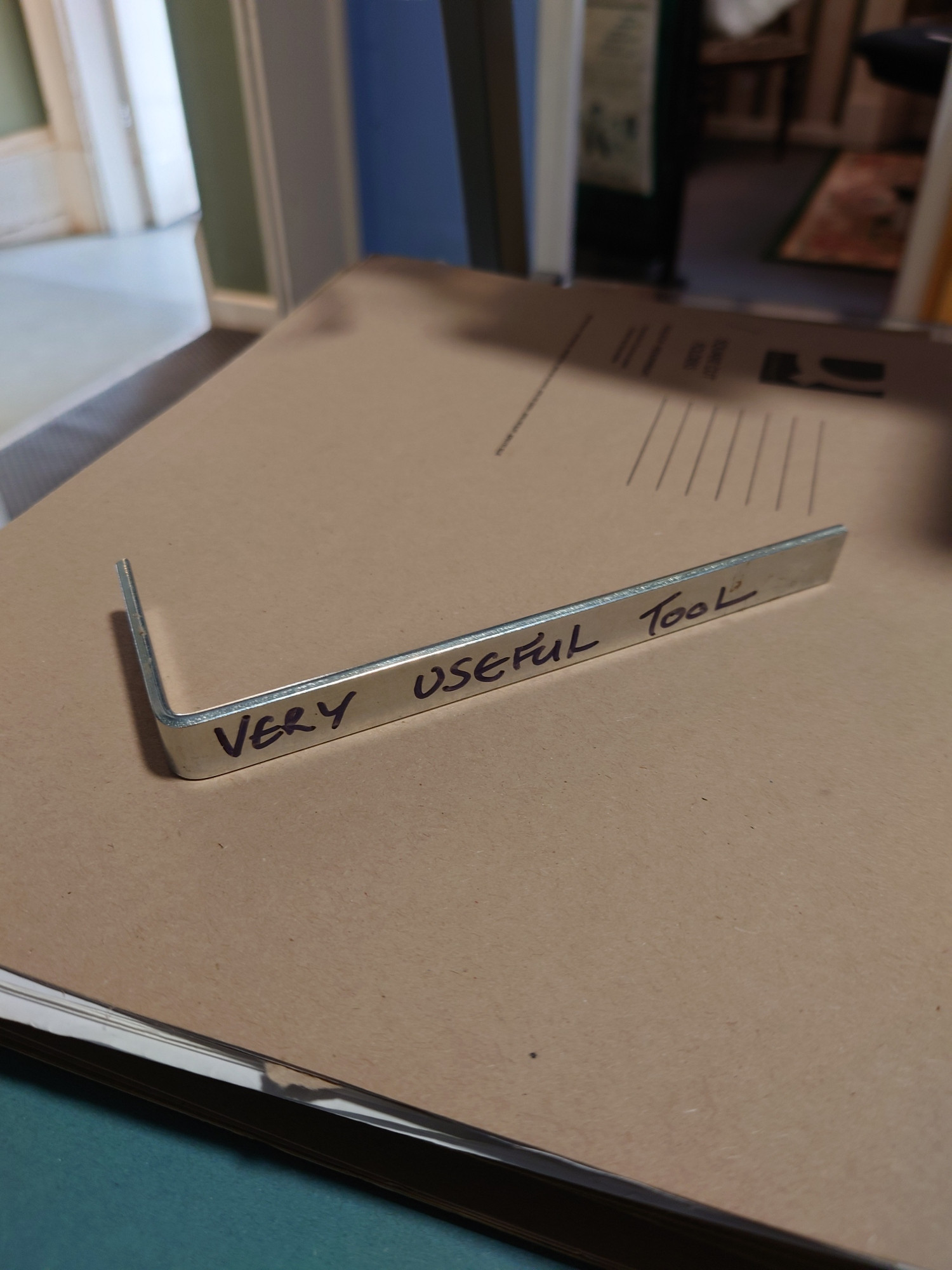 A piece of L-shaped metal with the words Very Useful Tool inscribed in black pen 
