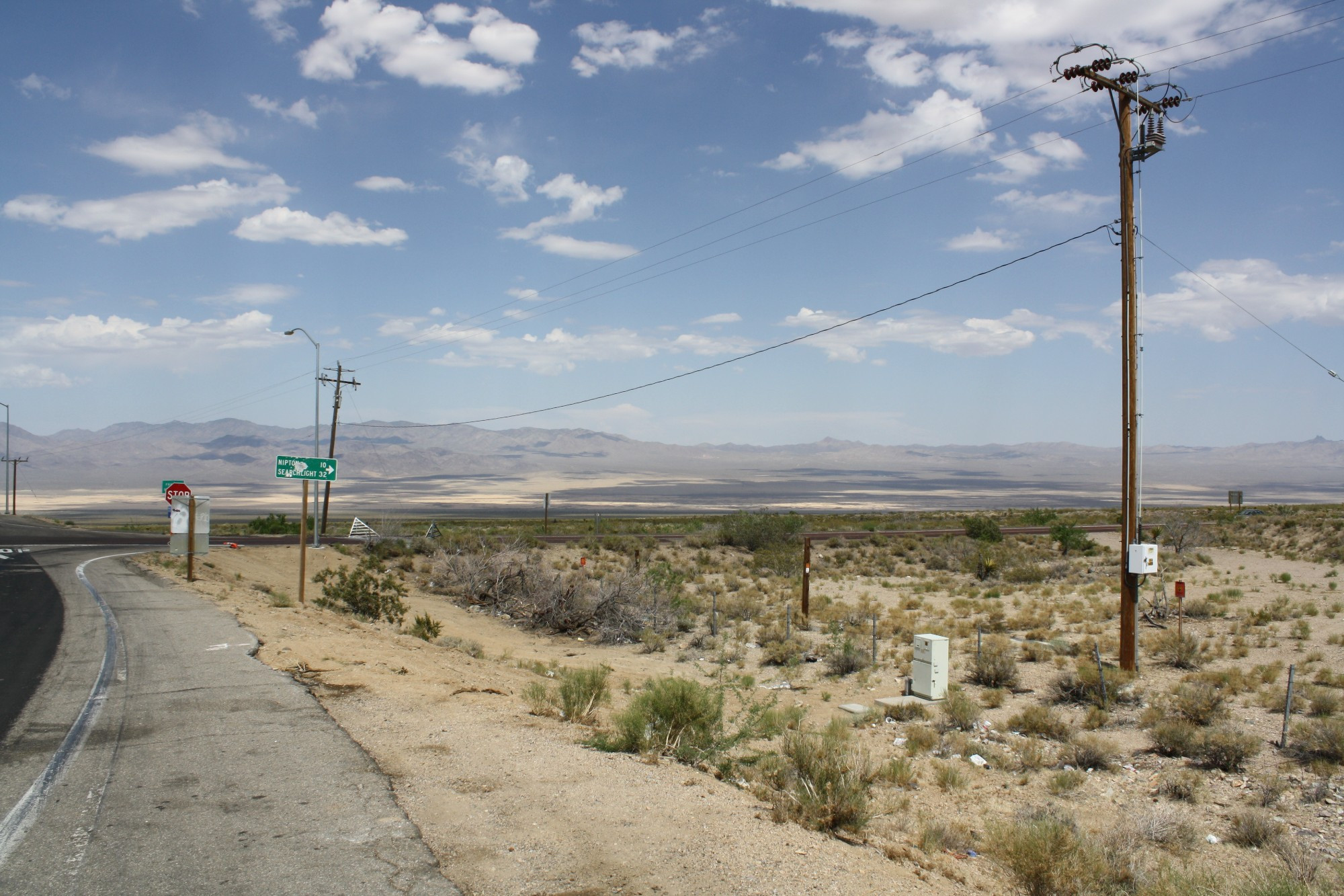 Desert highway photo with power lines (?) and a sign indicating distances to Nipton and Searchlight.