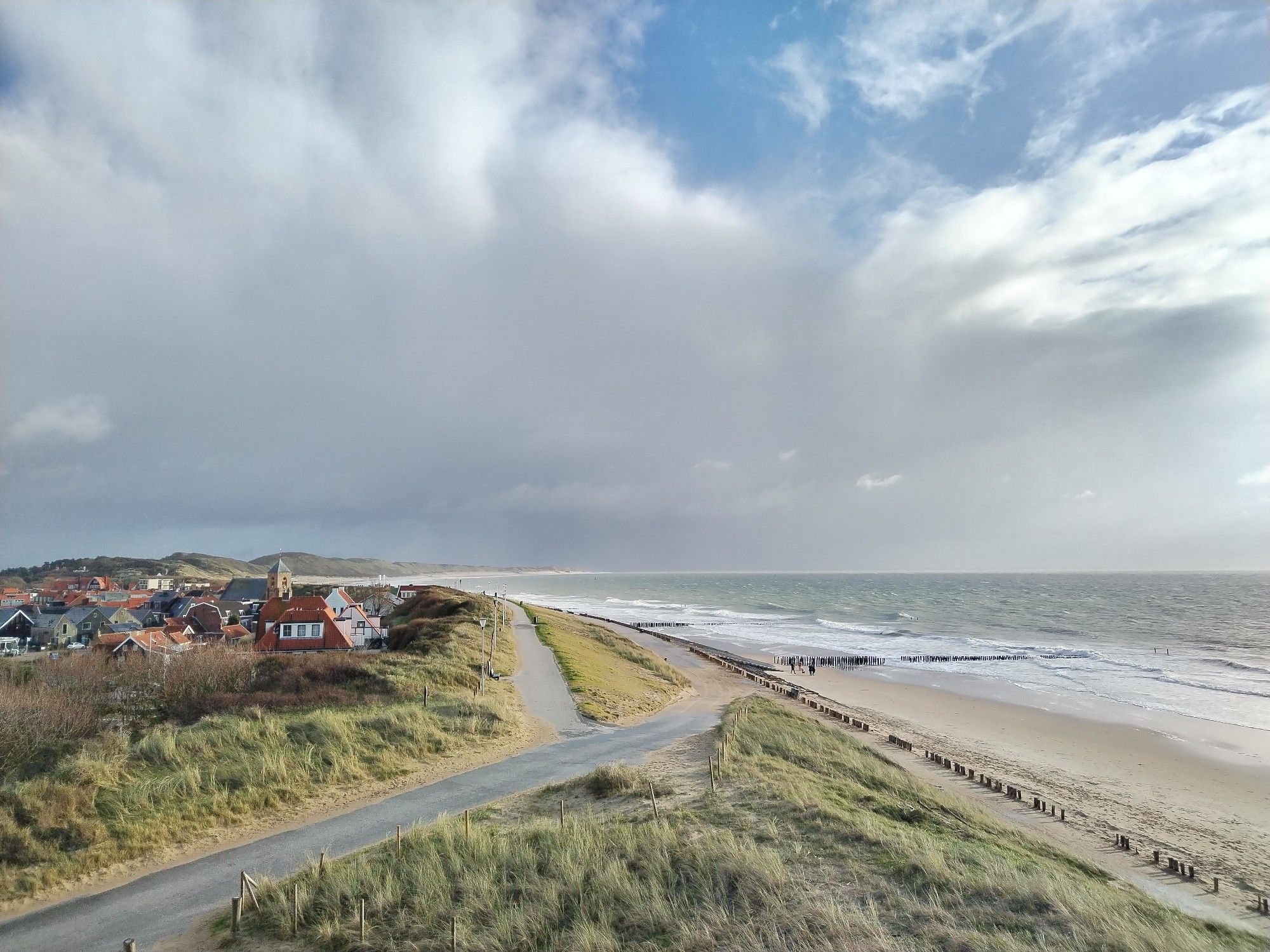 Blick auf eine Küstenlinie. Links ein kleines Dorf, rechts Strand und Meer.