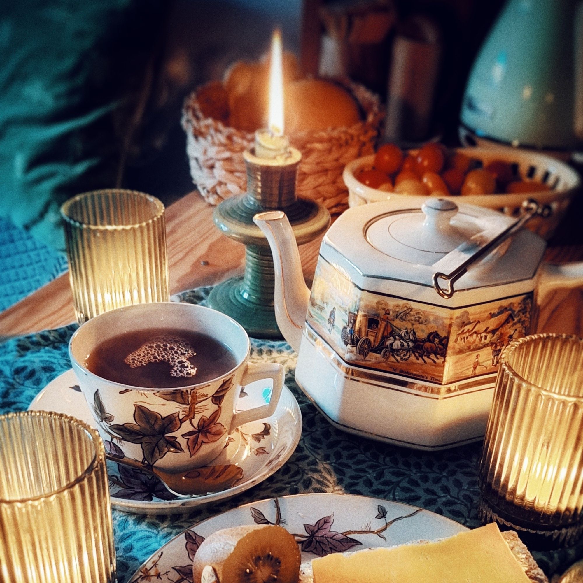 Une tasse de thé et une théière entourée de bougies et de fruits. C'est le matin.