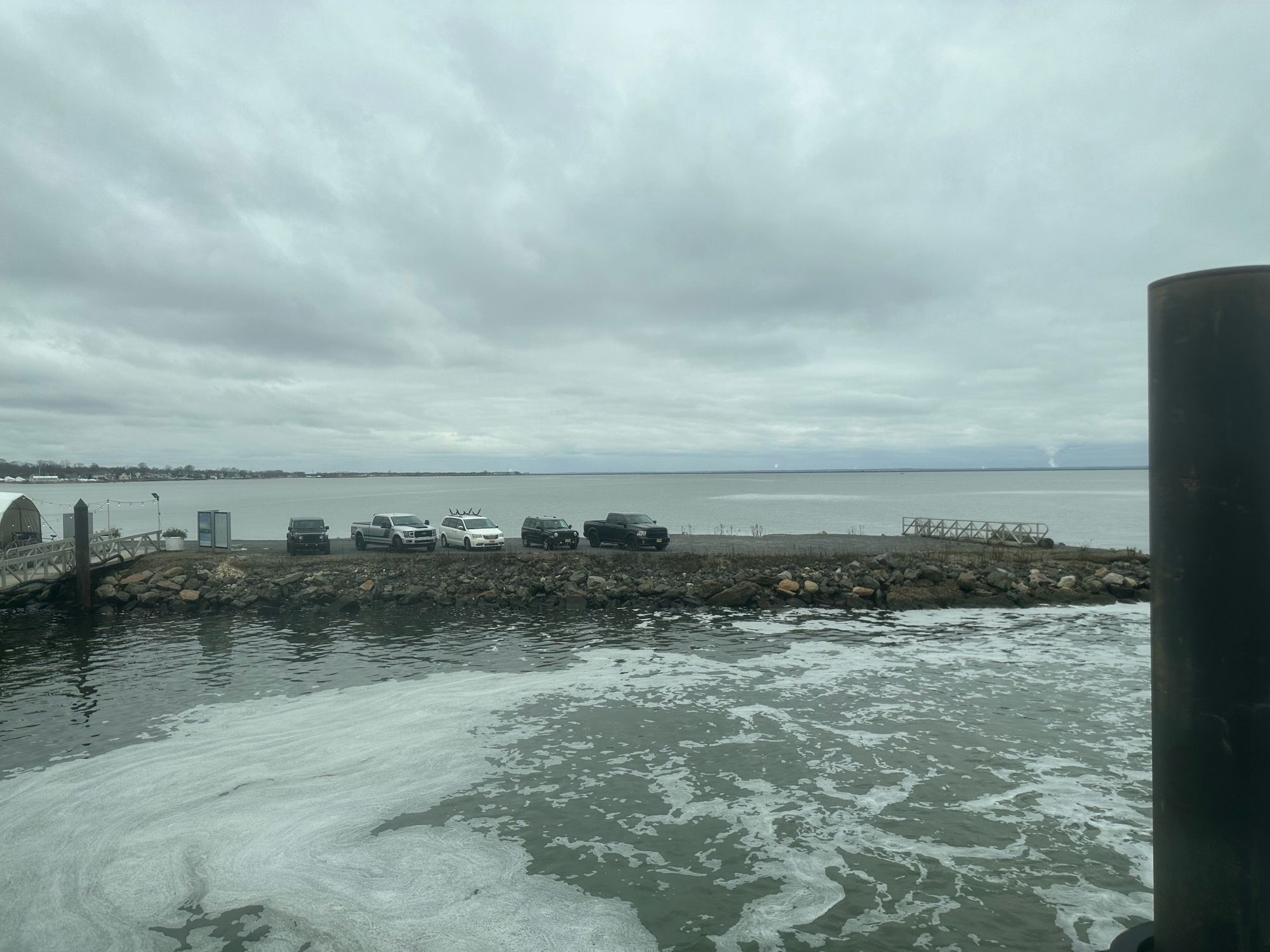 Turbulent waters on front of a jetty with a few vehicles parked on it.