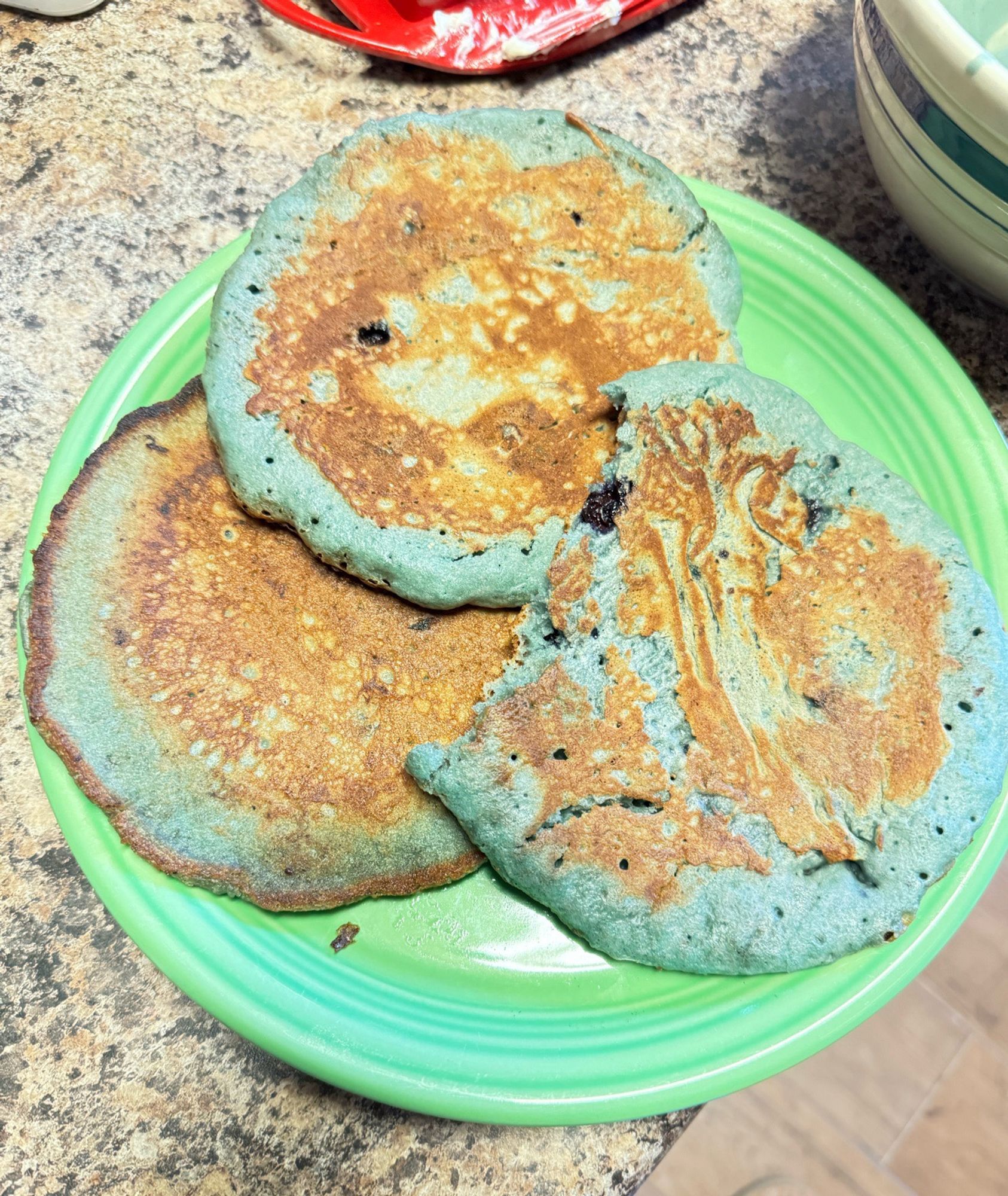 Three light blue pancakes on a green plate.