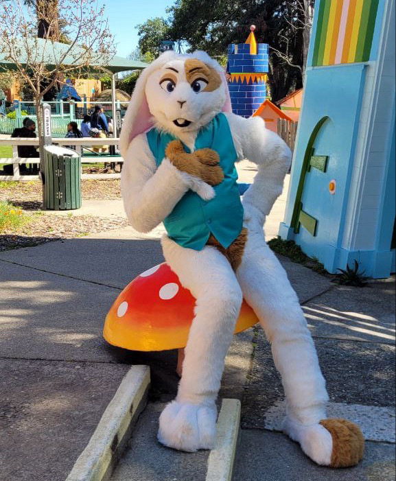 Nilla Bean, white & tan bunny, wearing an aquamarine vest, sitting on a mushroom