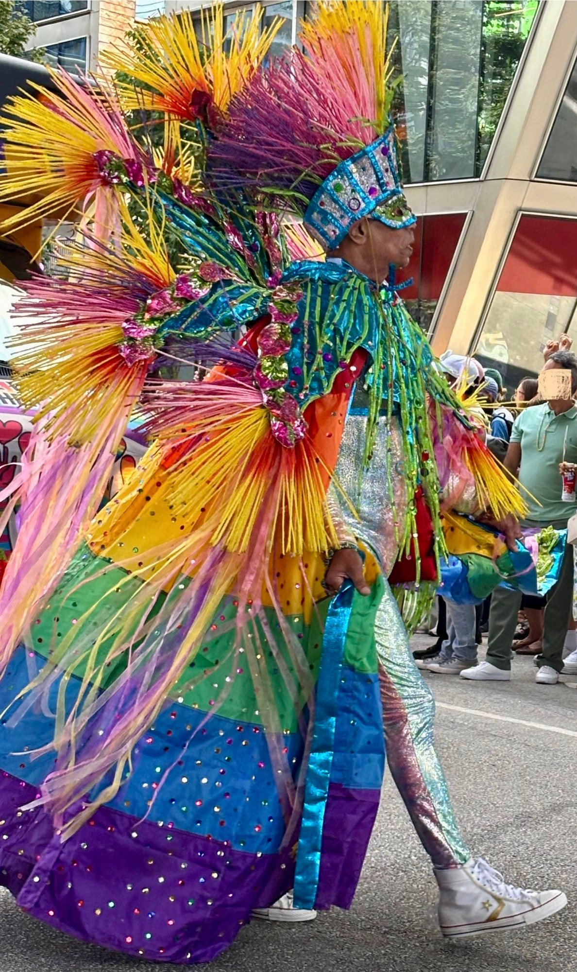 A man wearing a costume with pride colours.  Feathery and shiny and sparkly, hard to describe 