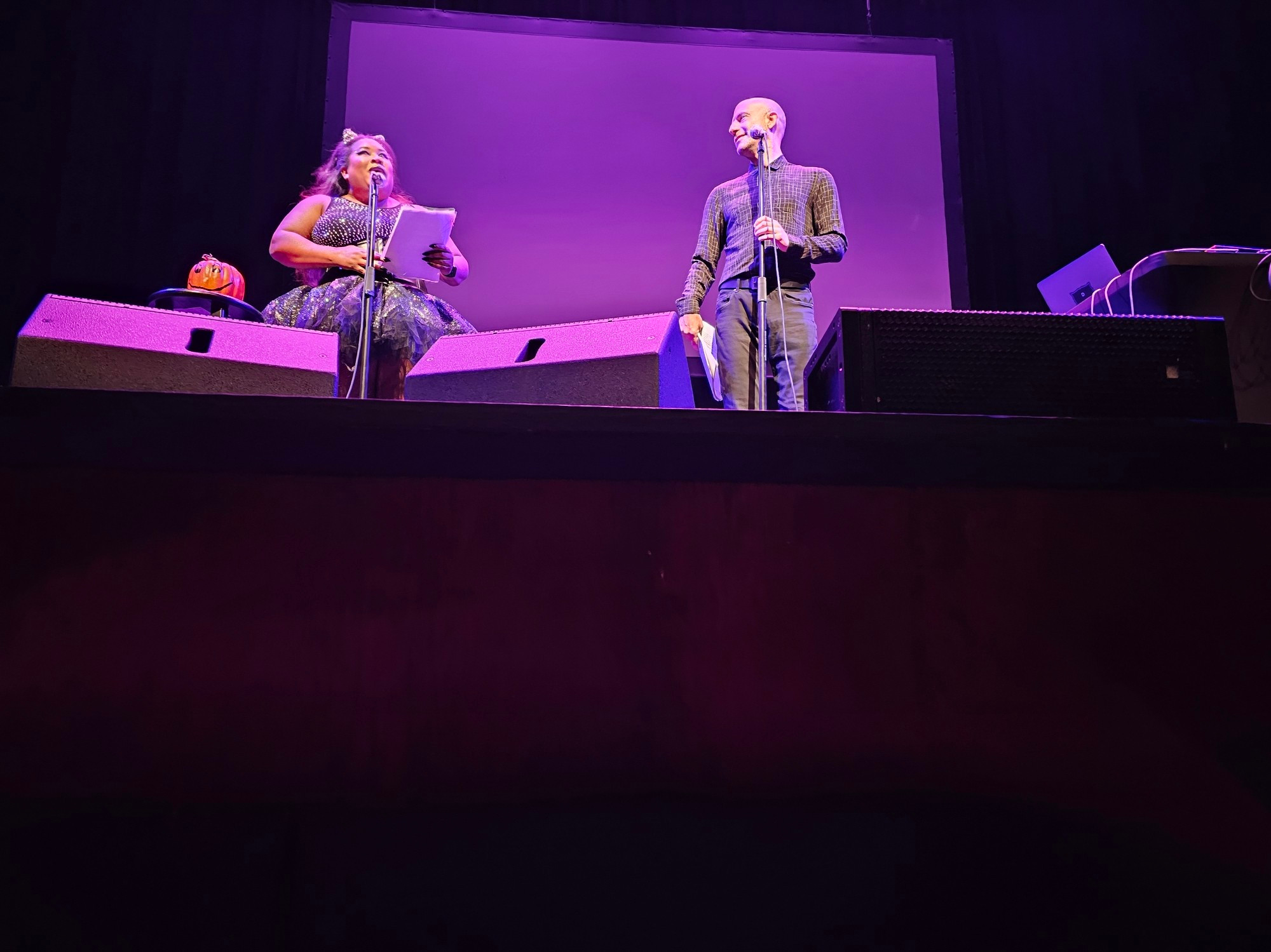 The actor Cecil Baldwin stands on a stage with purple lighting. To his right stands actress Symphony Sanders.