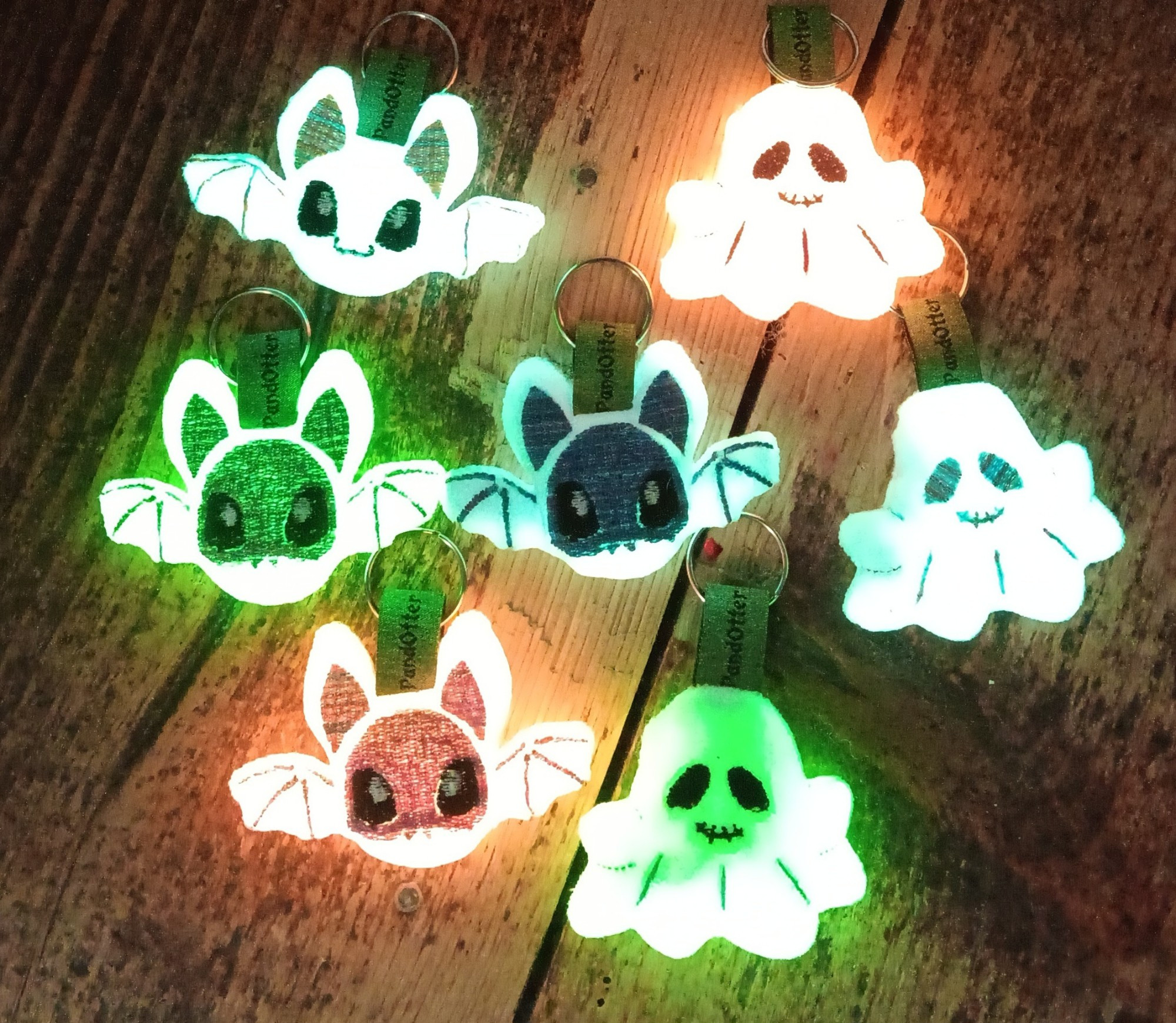 4 Bat charms and 3 cute Ghost charms in the dark, laying at a wodden floor. Due to the glow in the dark minky they are made of, the are glowing very bright.