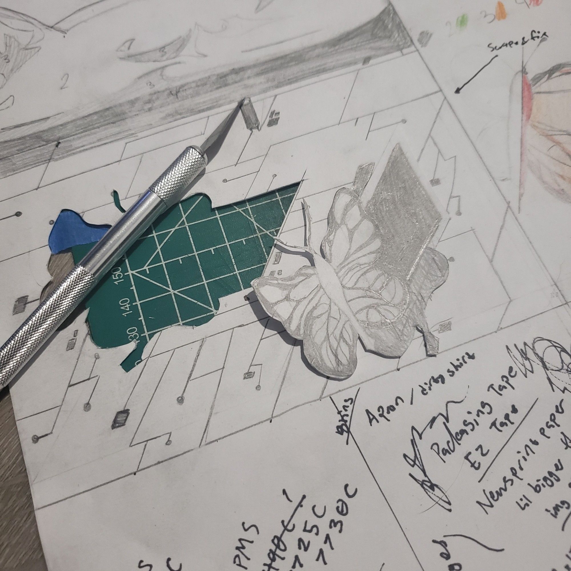 An x-acto knife laying next to a cut-out hole. A cut-out of a butterfly and a square resembling a CPU chip sit aside.