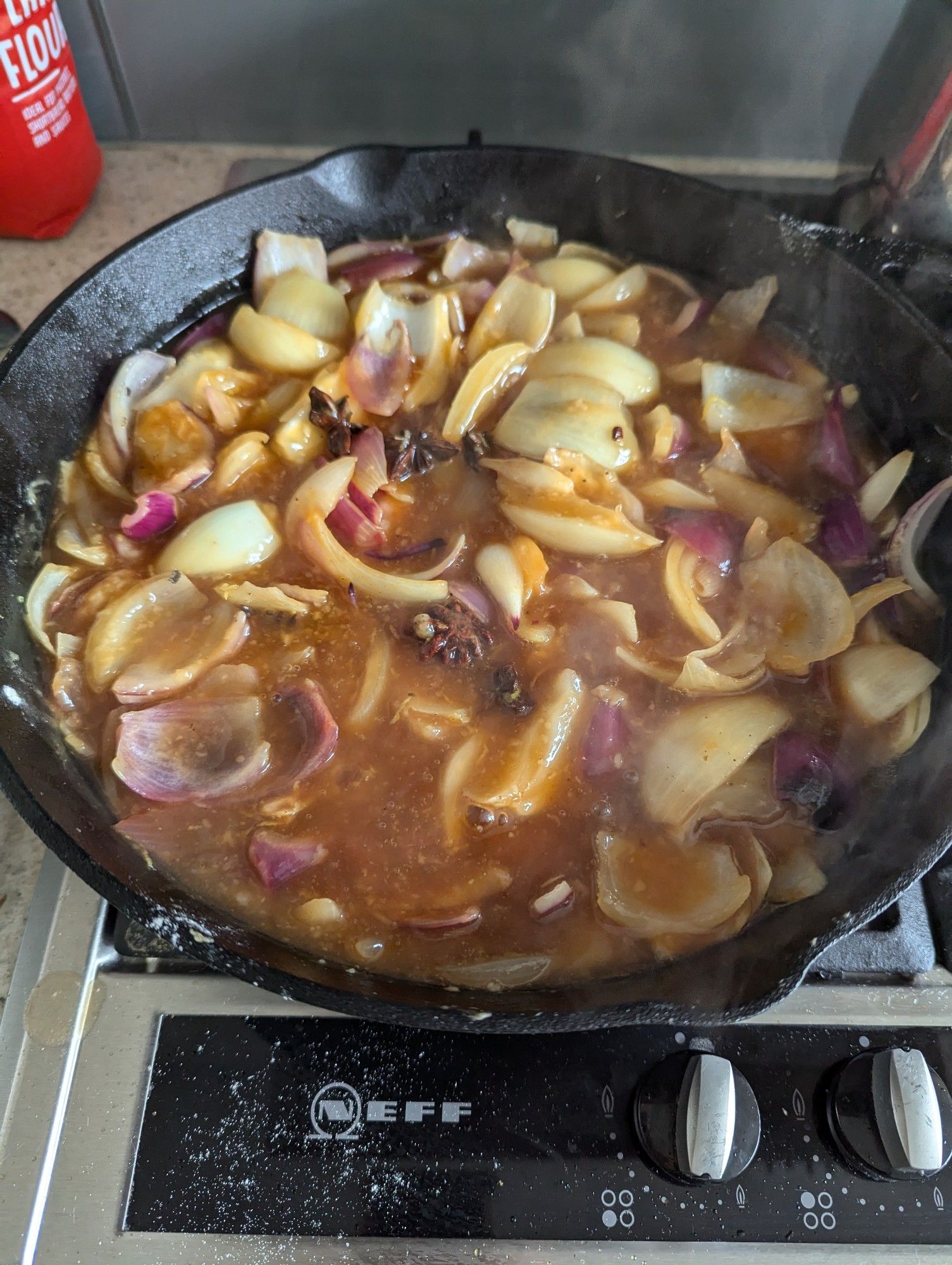 Onions cooking in the cast iron skillet with star anise, lemon zest, lemon and lime juice, soy sauce, plum sauce and chicken stock