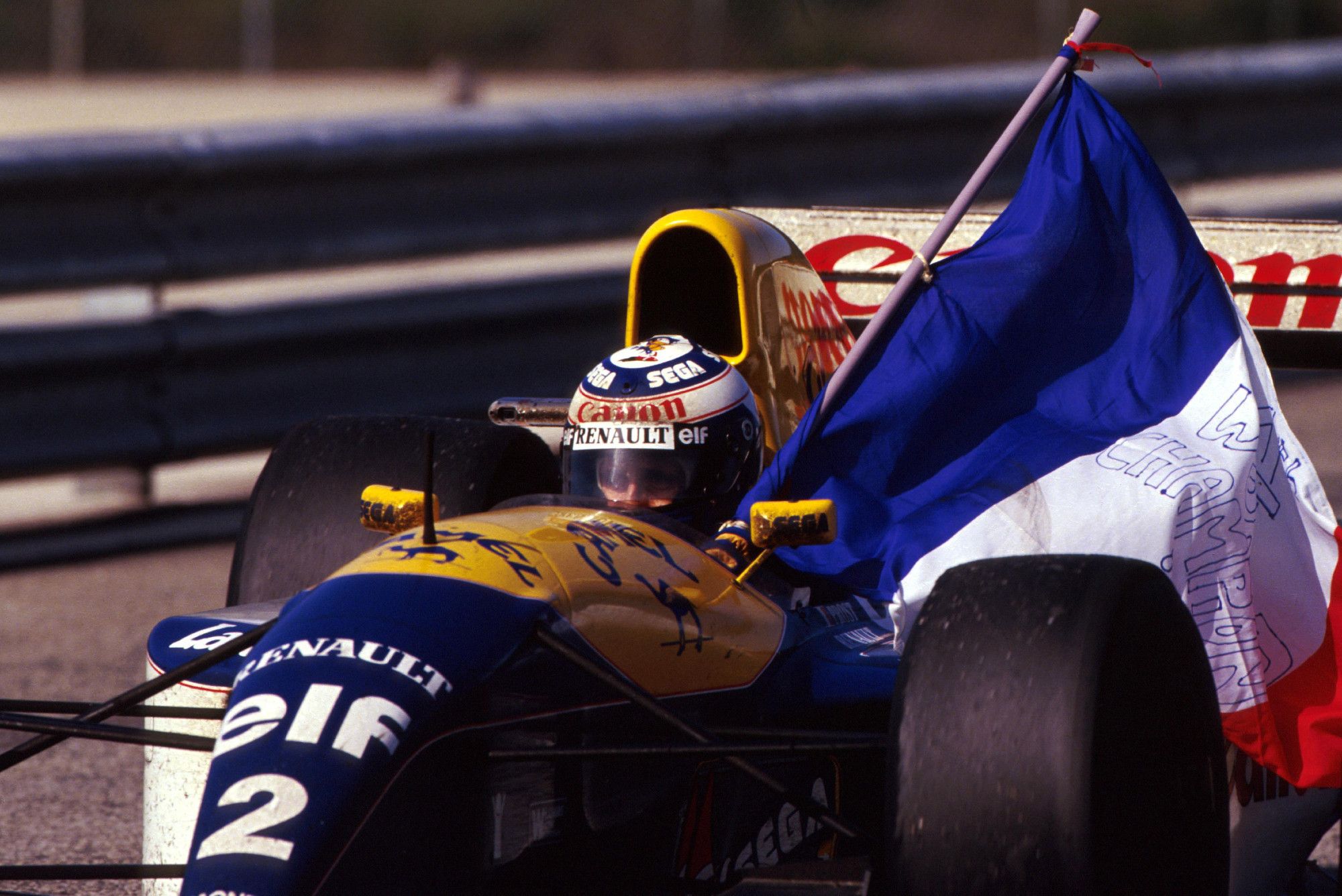 Picture of Alain Prost driving a Williams while carrying the French flag in his car.