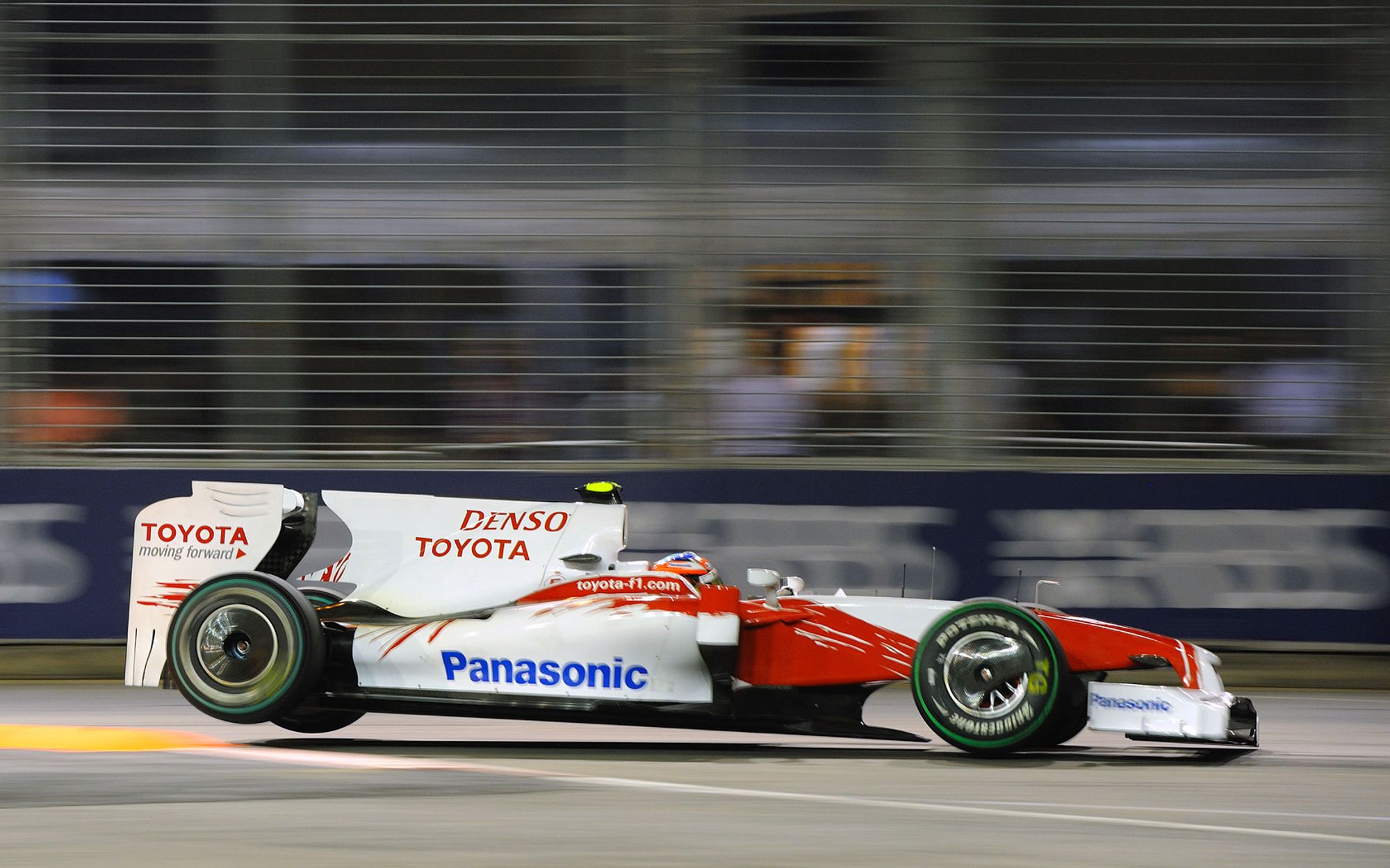 Photo of Timo Glock, seen from the side, driving over kerbs in night-time Marina Bay.