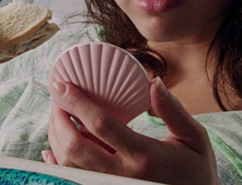 a person is holding a pink clam shell e-reader or phone and holding it close to their chin