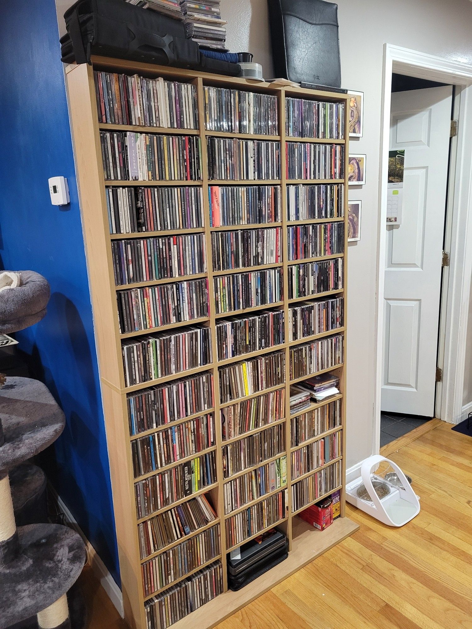 Photo of a 12 row, 3 column CD rack chock full of CDs, with more stacked on top, situated around the corner from the blue wall you'll recognize from the media center photo in the prior skeet.