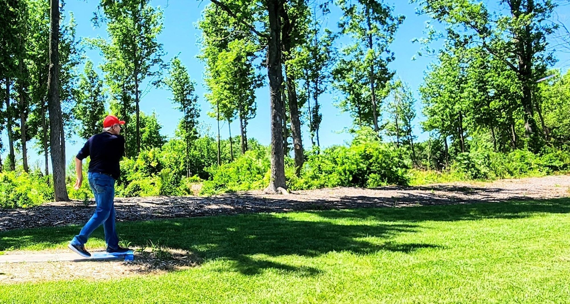 L to R shot of a man playing disc golf. He's just thrown a disc which is barely visible on the extreme right.