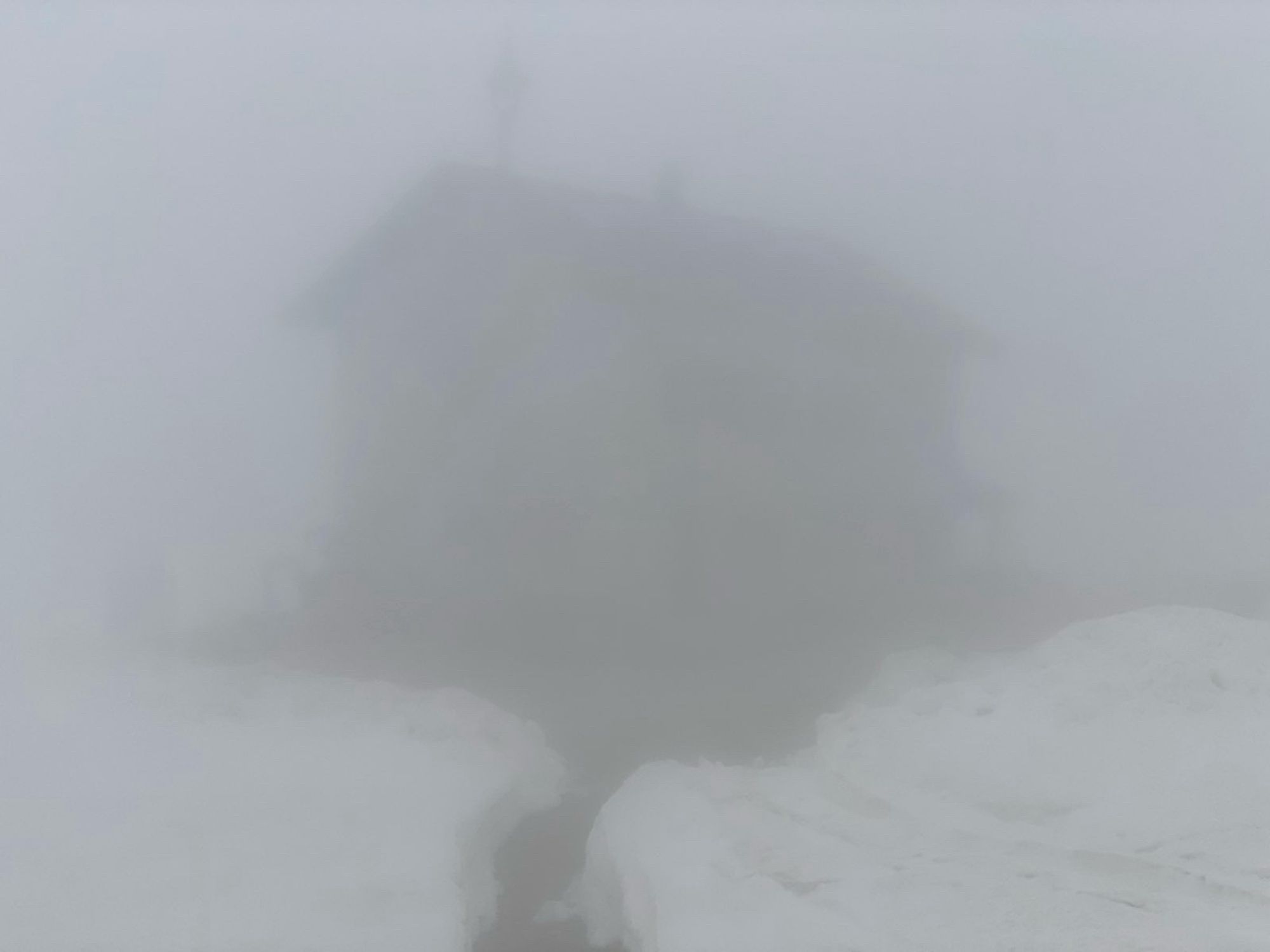 Nebel, ganz undeutlich eine Hütte im Schnee