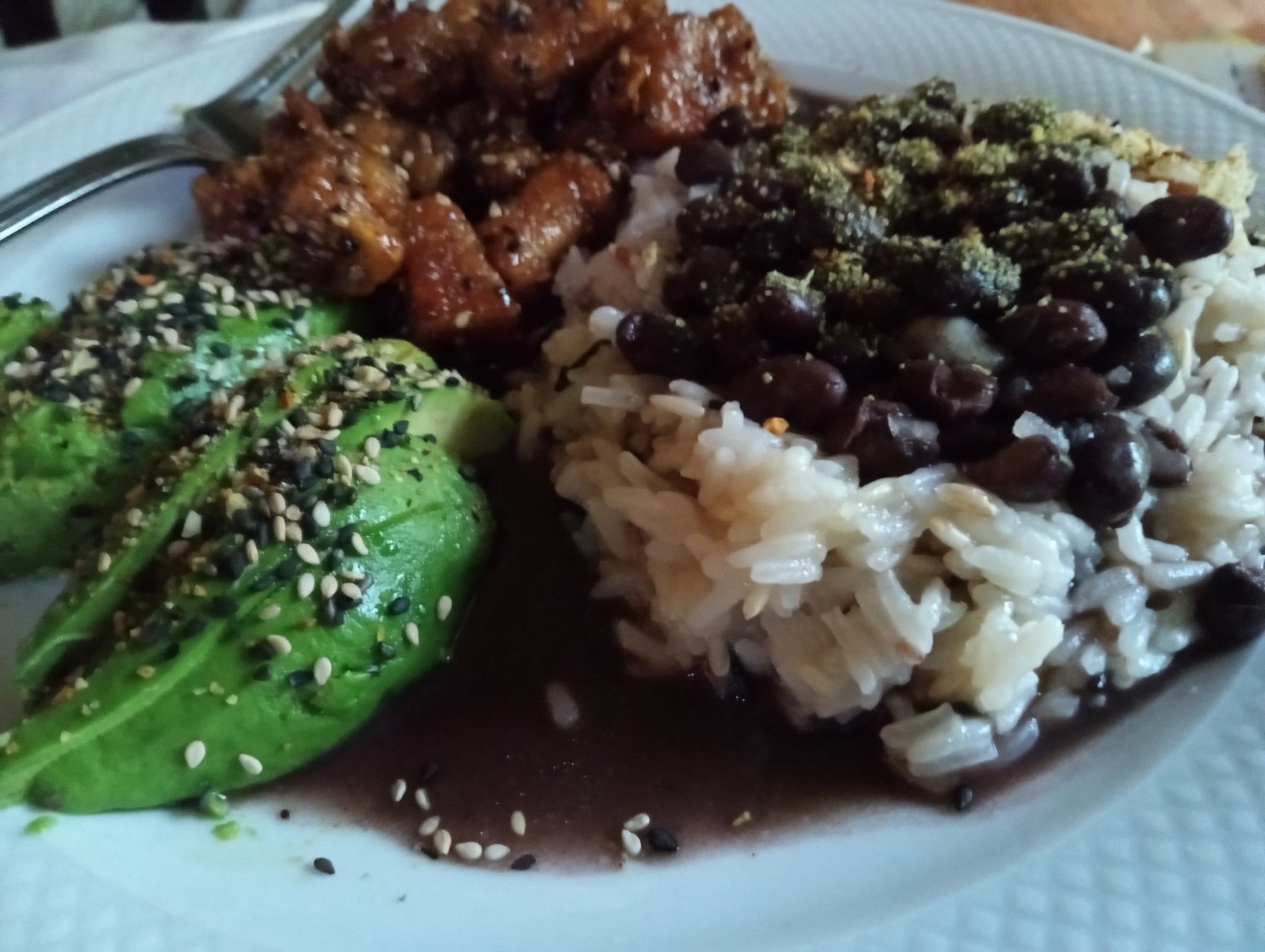 A white dinner plate with white jasmine rice on the right and it is topped with black beans. On the left is sliced avocado and sauteed tofu.