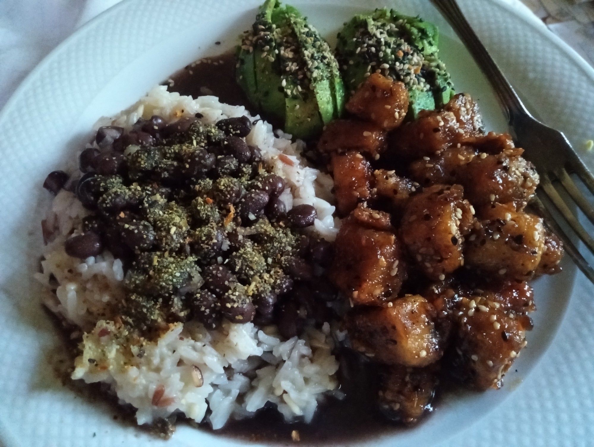 A white dinner plate with white jasmine rice on the left and it is topped with black beans. On the right is sliced avocado and sauteed tofu.